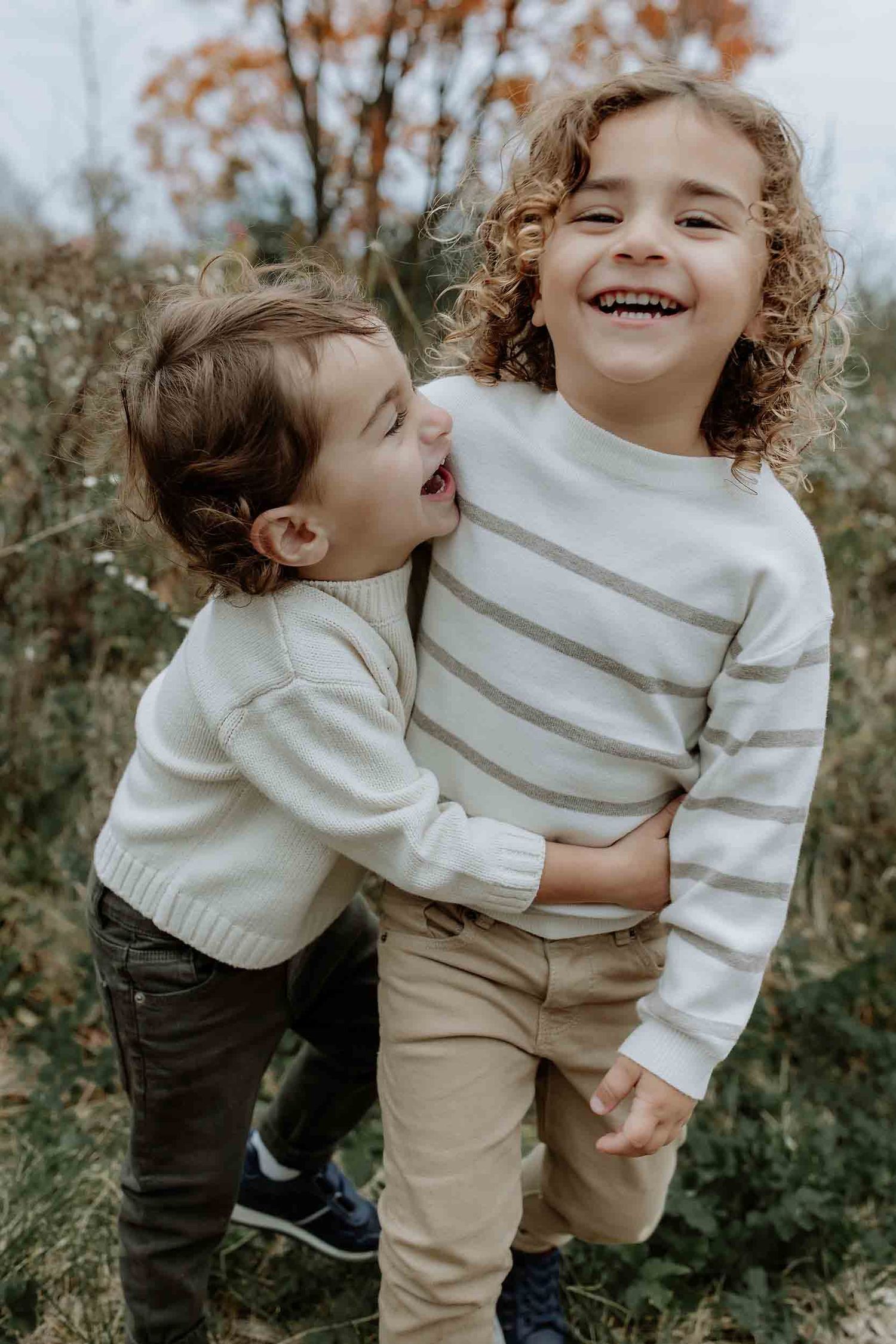 Two children sharing laughter and hugs outdoors in autumn setting.