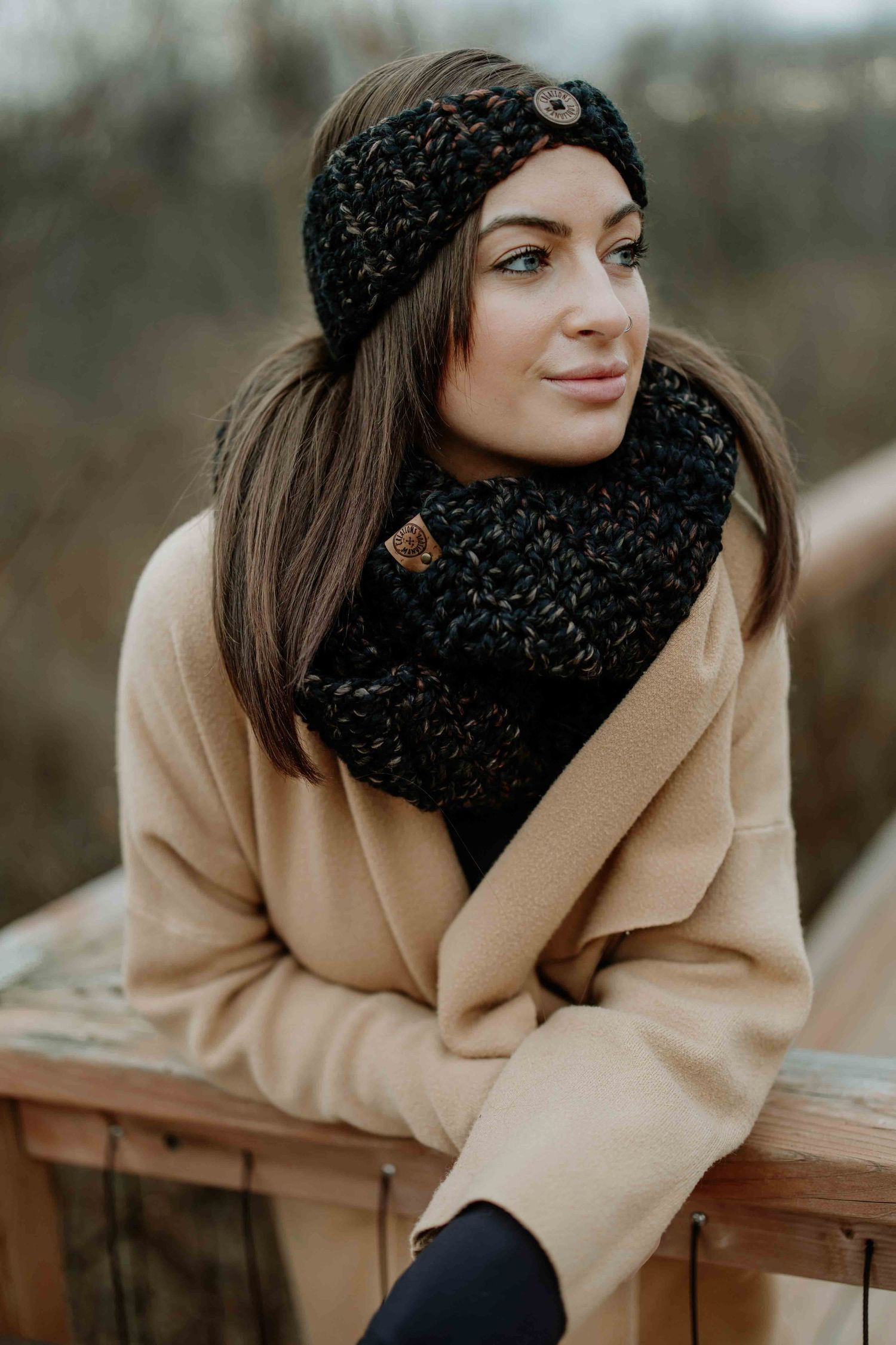 Person in beige coat and black winter hat leaning on wooden railing outdoors.