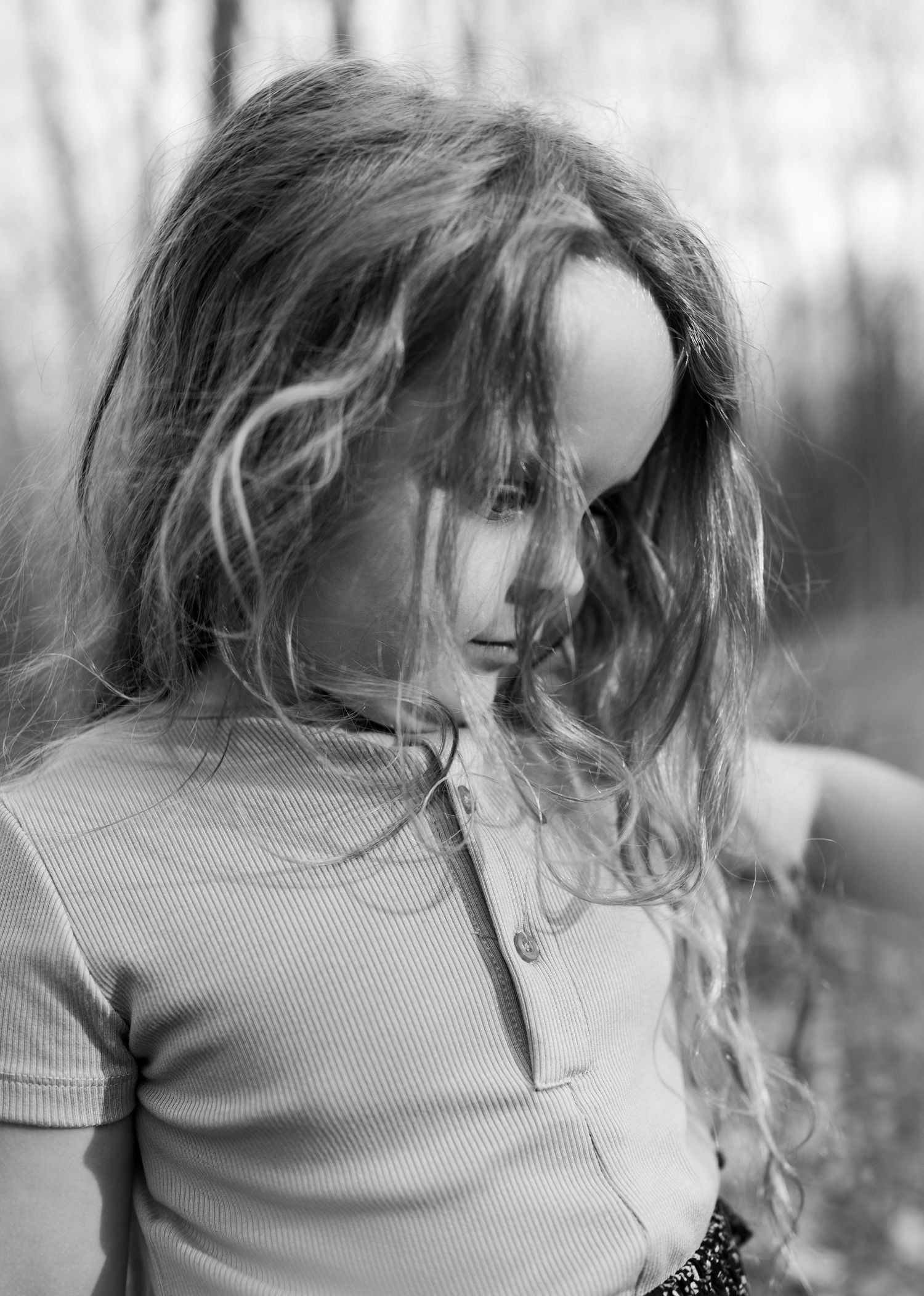 Black and white portrait of a young girl with long wavy hair blowing in the wind outdoors.