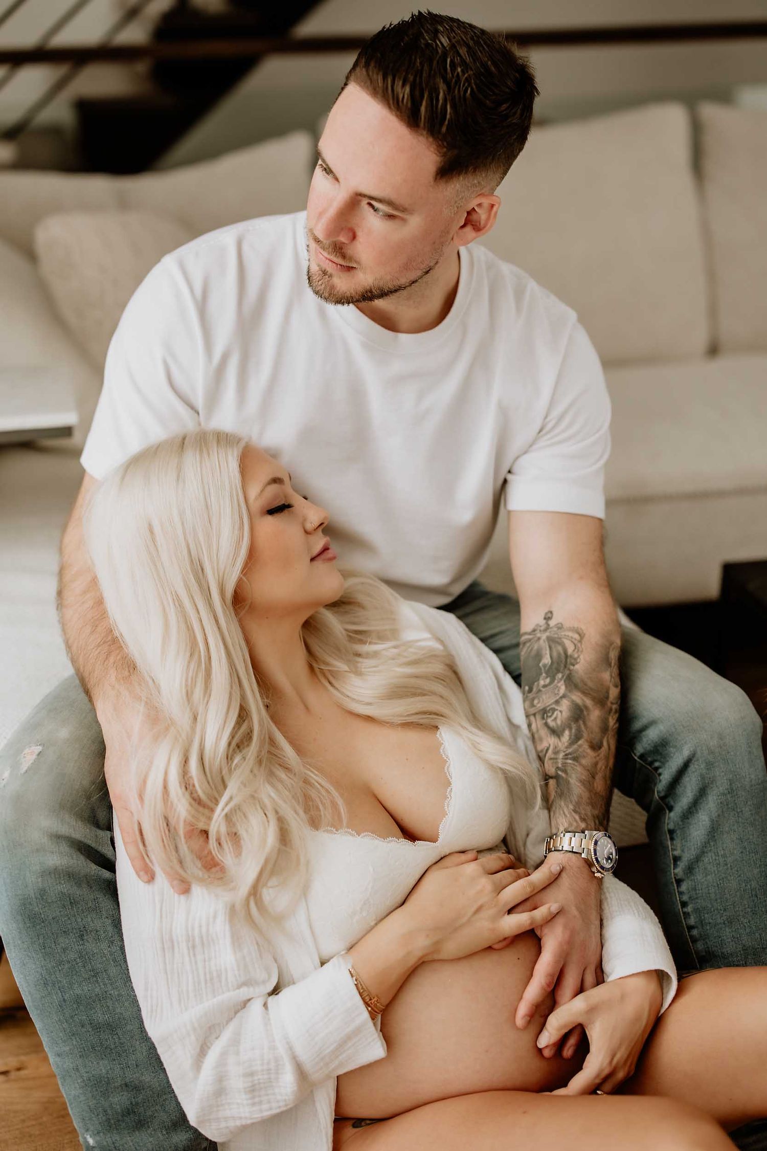 Intimate couple's portrait session on a grey couch in natural lighting.