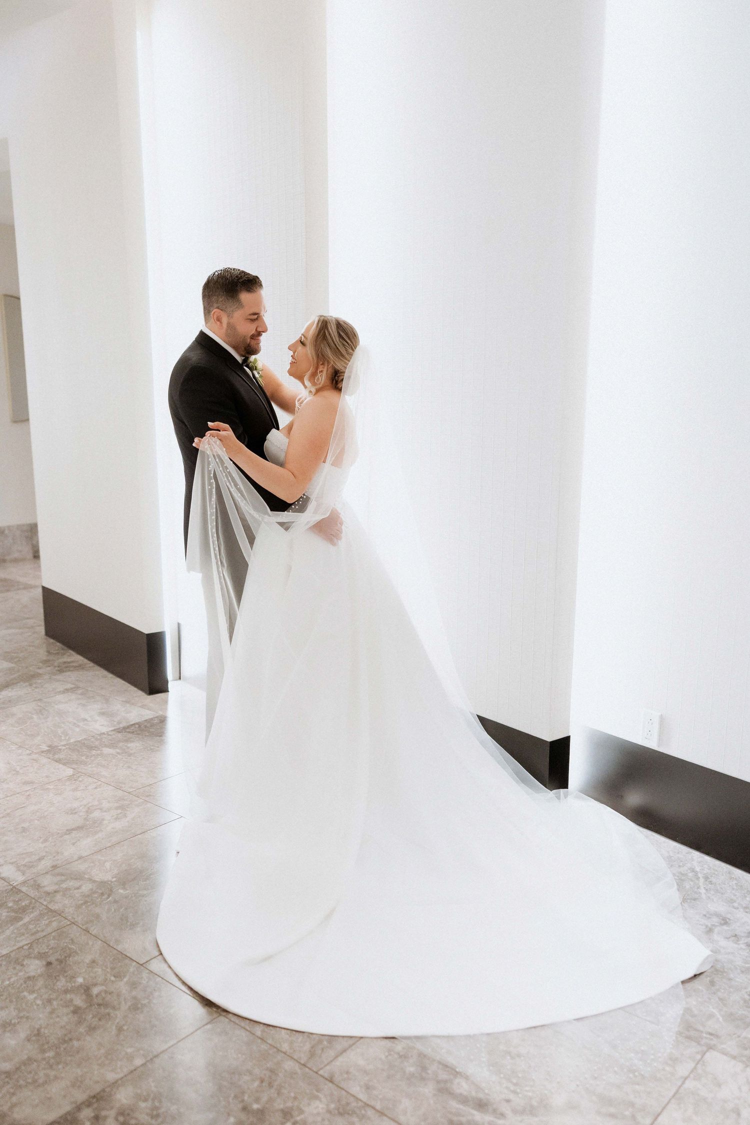 Elegant full-length wedding portrait of a couple against white pillars showing the bride's dramatic train.