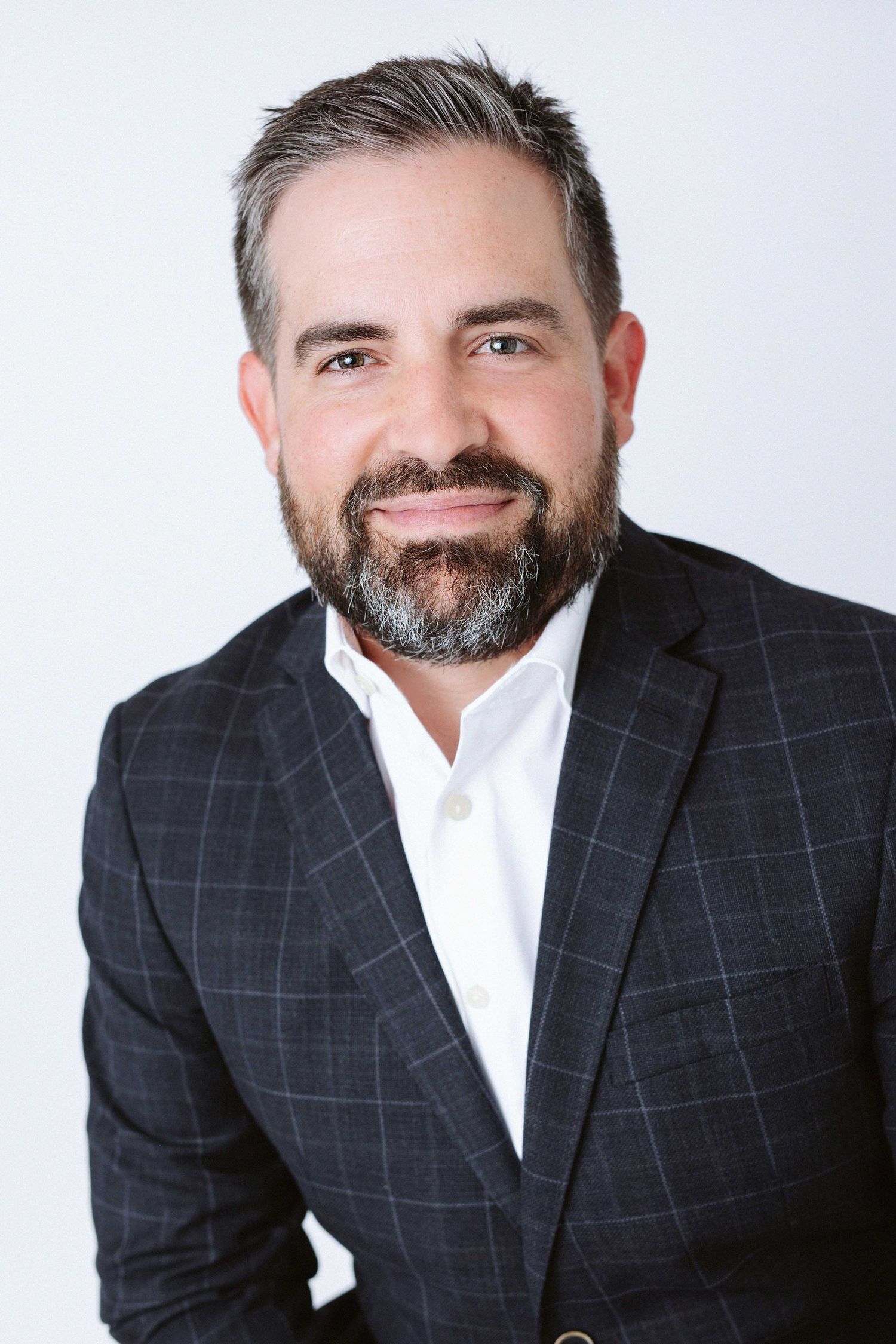 Professional headshot of person wearing checkered blazer against white background.