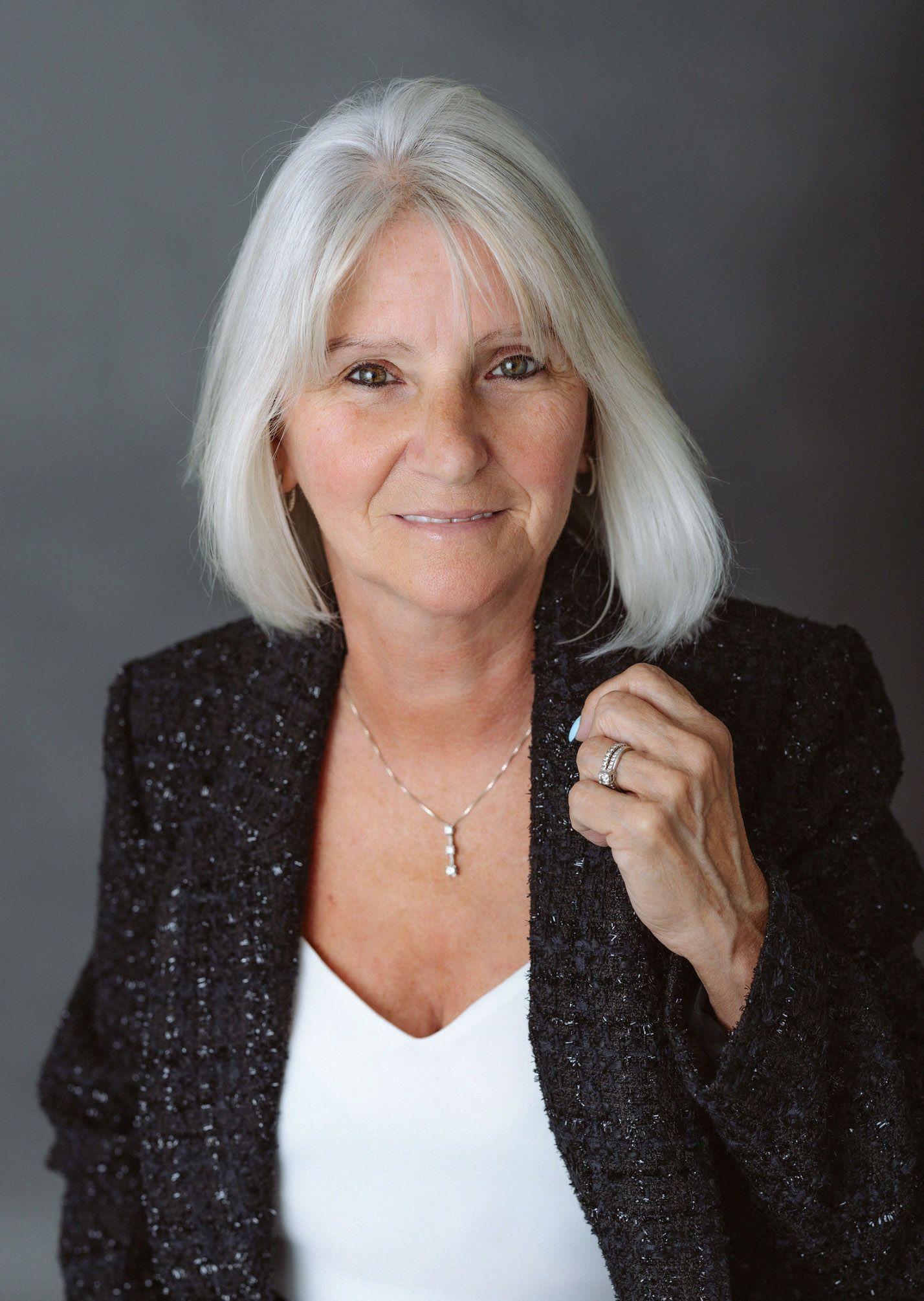 Studio portraits of person in black blazer and white top against dark background.