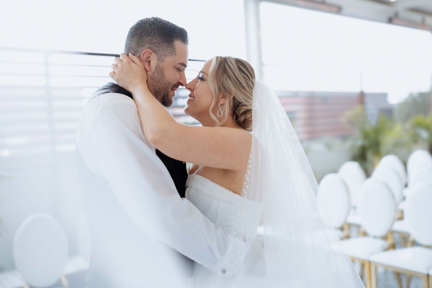 Wedding couple shares intimate moments in a bright, airy venue with white decor and natural lighting.