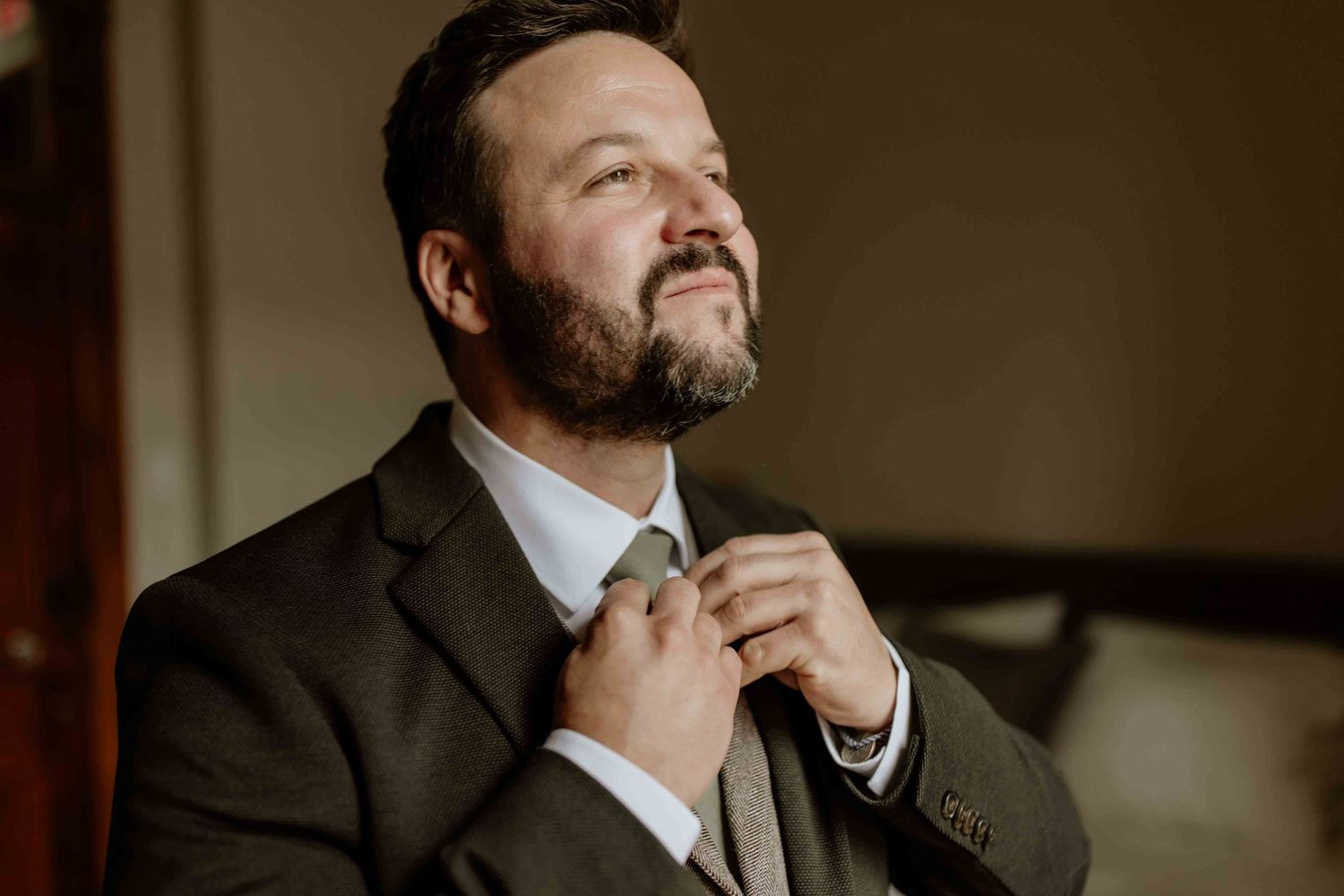 Moody portrait shots of groom getting ready in warm lighting.