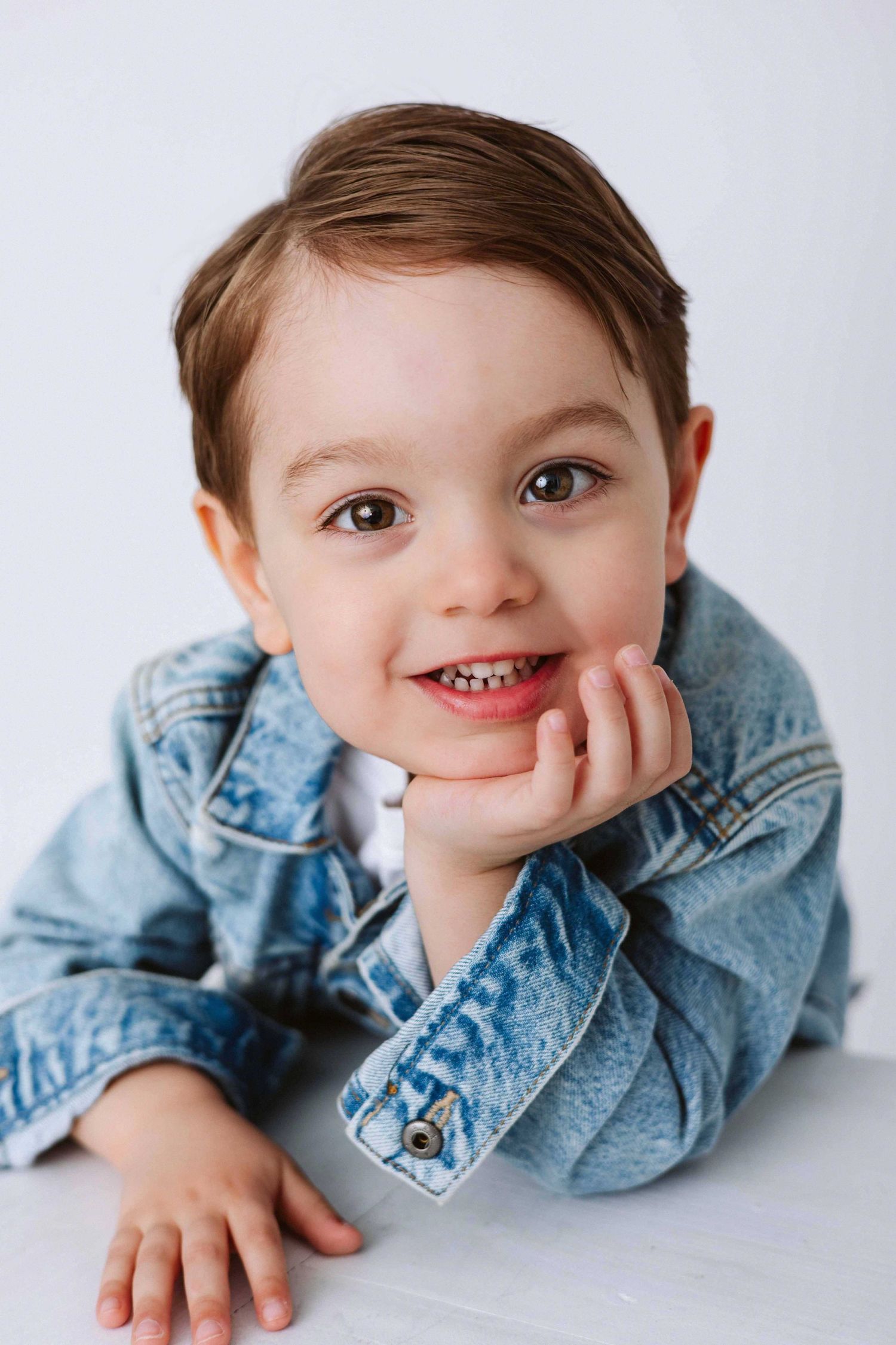Young person in denim jacket lying down and smiling during playful studio photoshoot.