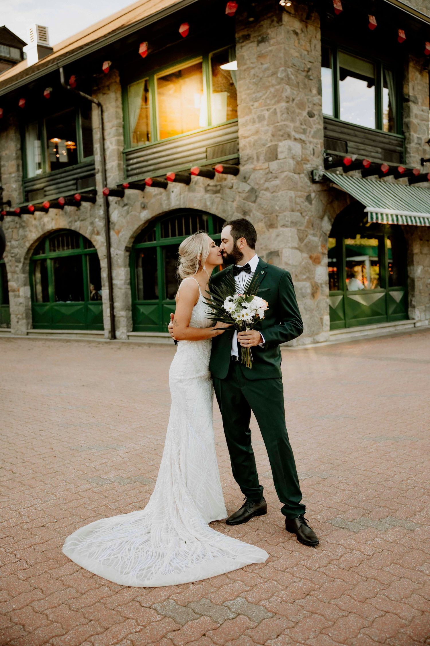 Romantic wedding couple shares intimate moments on stone patio with string lights at sunset.