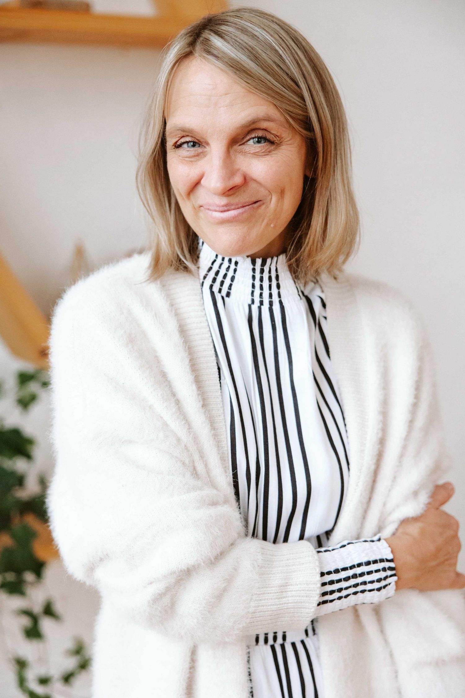 Person in cozy white sweater and striped top poses against light background.