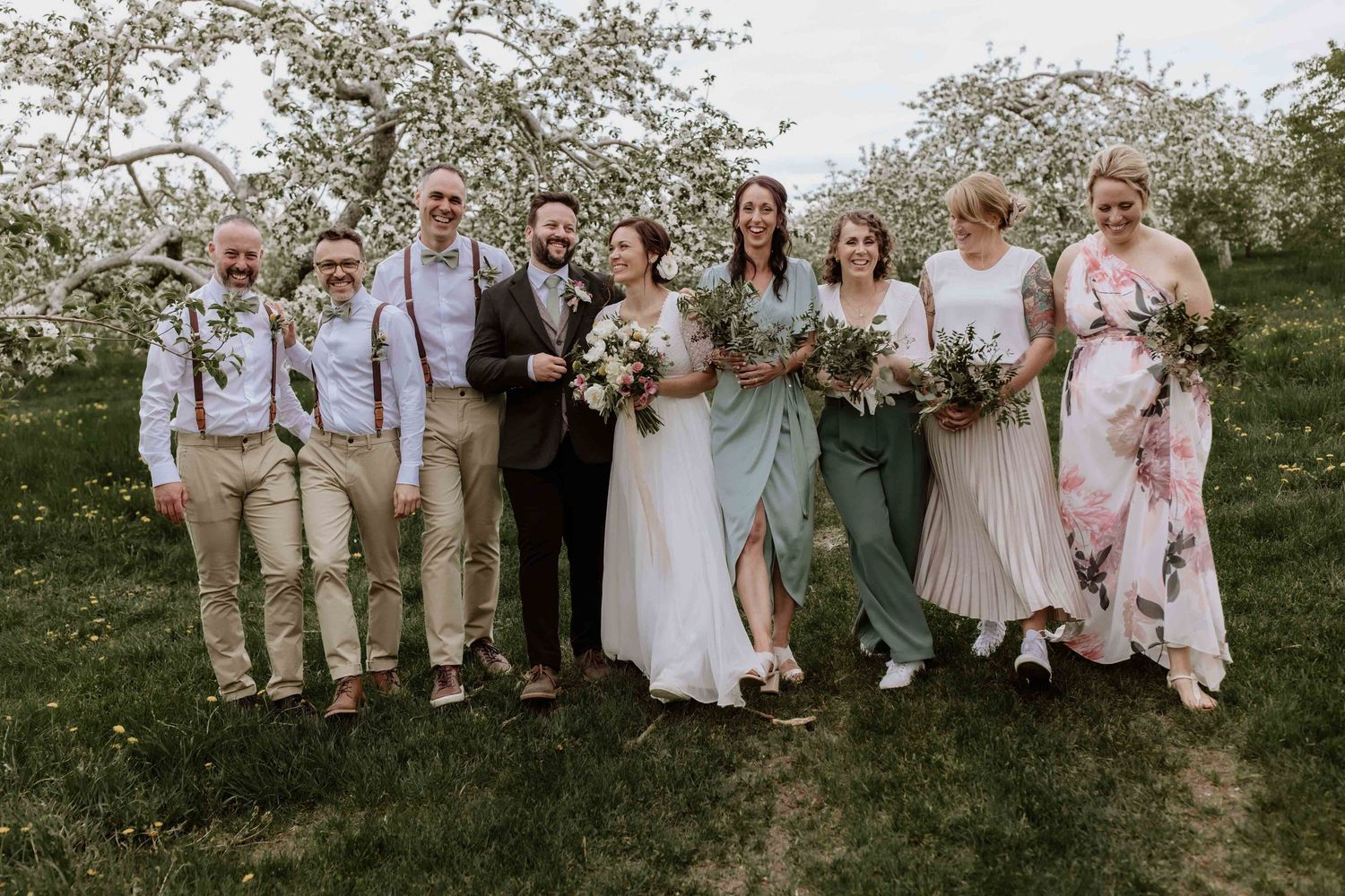 Wedding party group photo under blooming spring trees with casual attire.