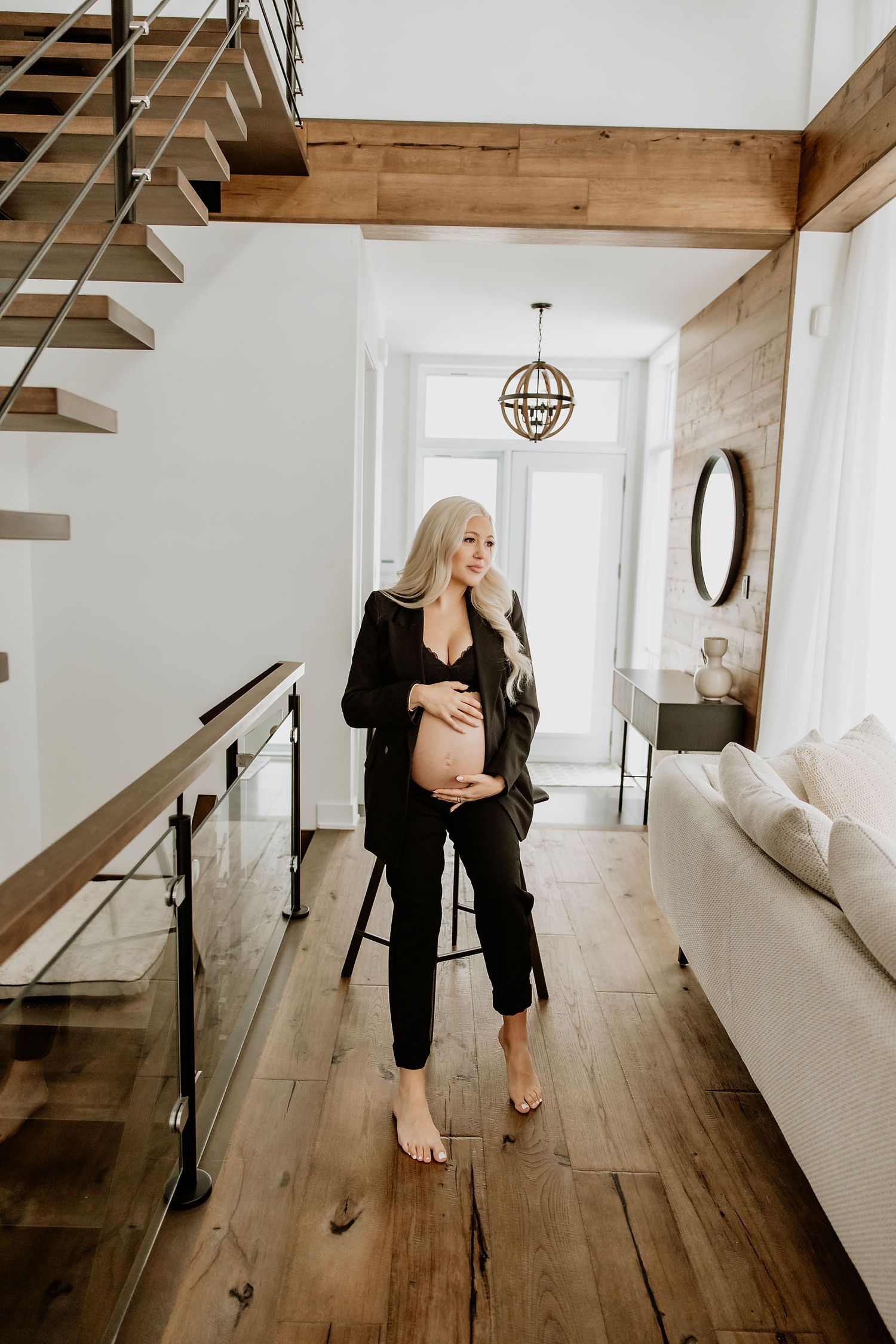 Woman in black outfit walking through modern interior with wooden floors and white walls.