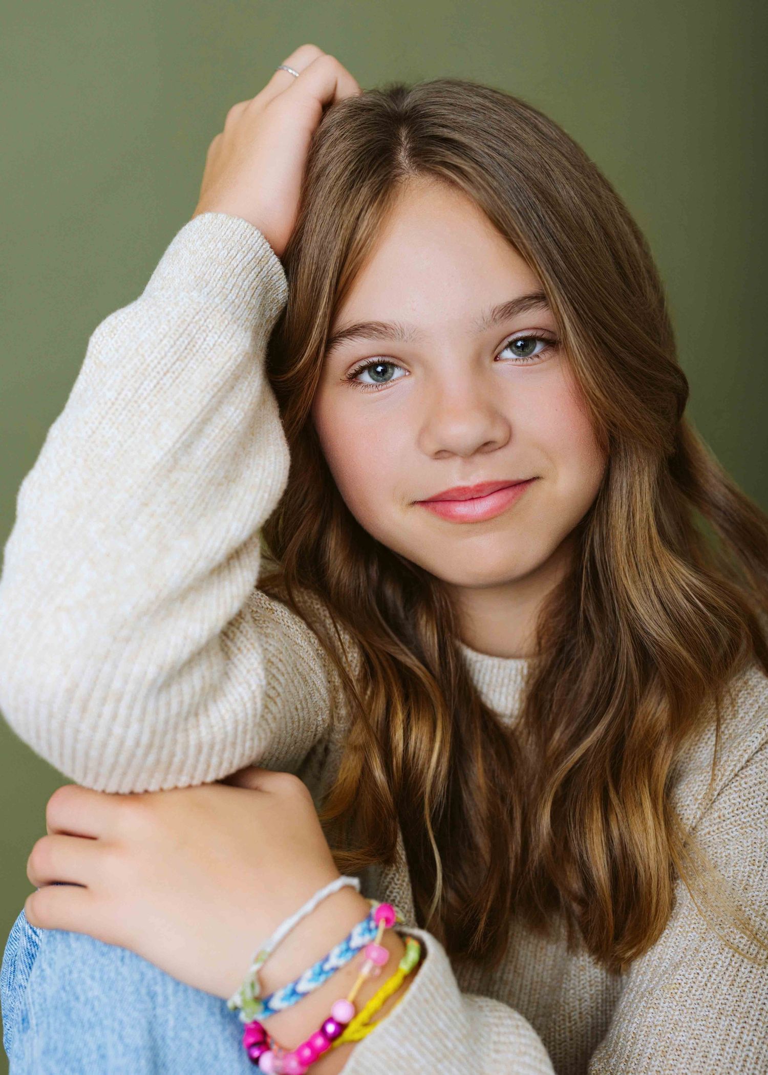 Casual portraits in cream sweater with colorful friendship bracelets against green background.