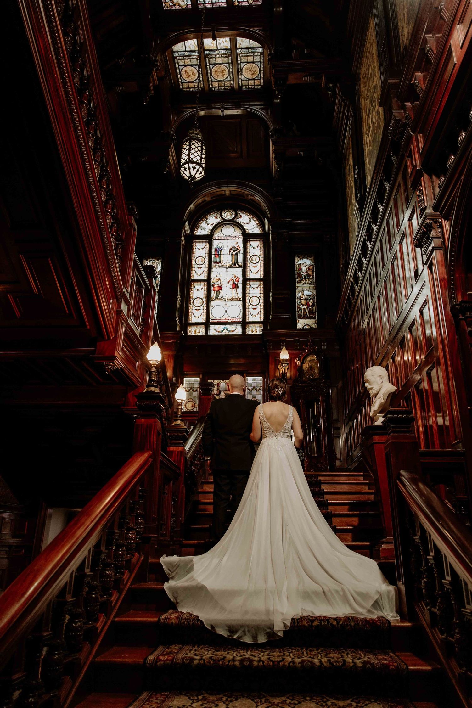 Dramatic wedding dress silhouette in dark church hallway with stained glass windows and ornate woodwork.