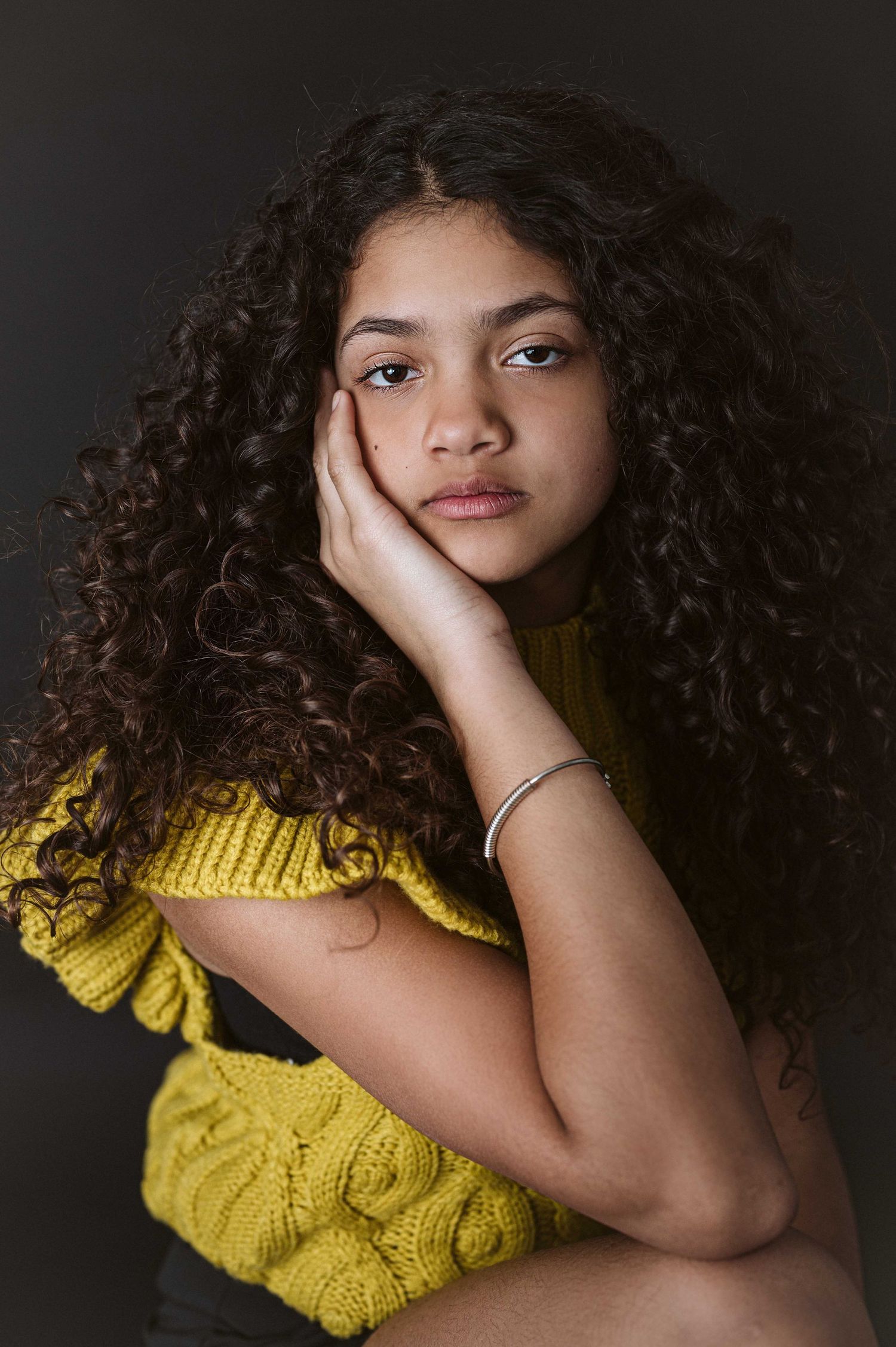 Portrait series featuring model in yellow sweater with curly hair against dark backdrop.