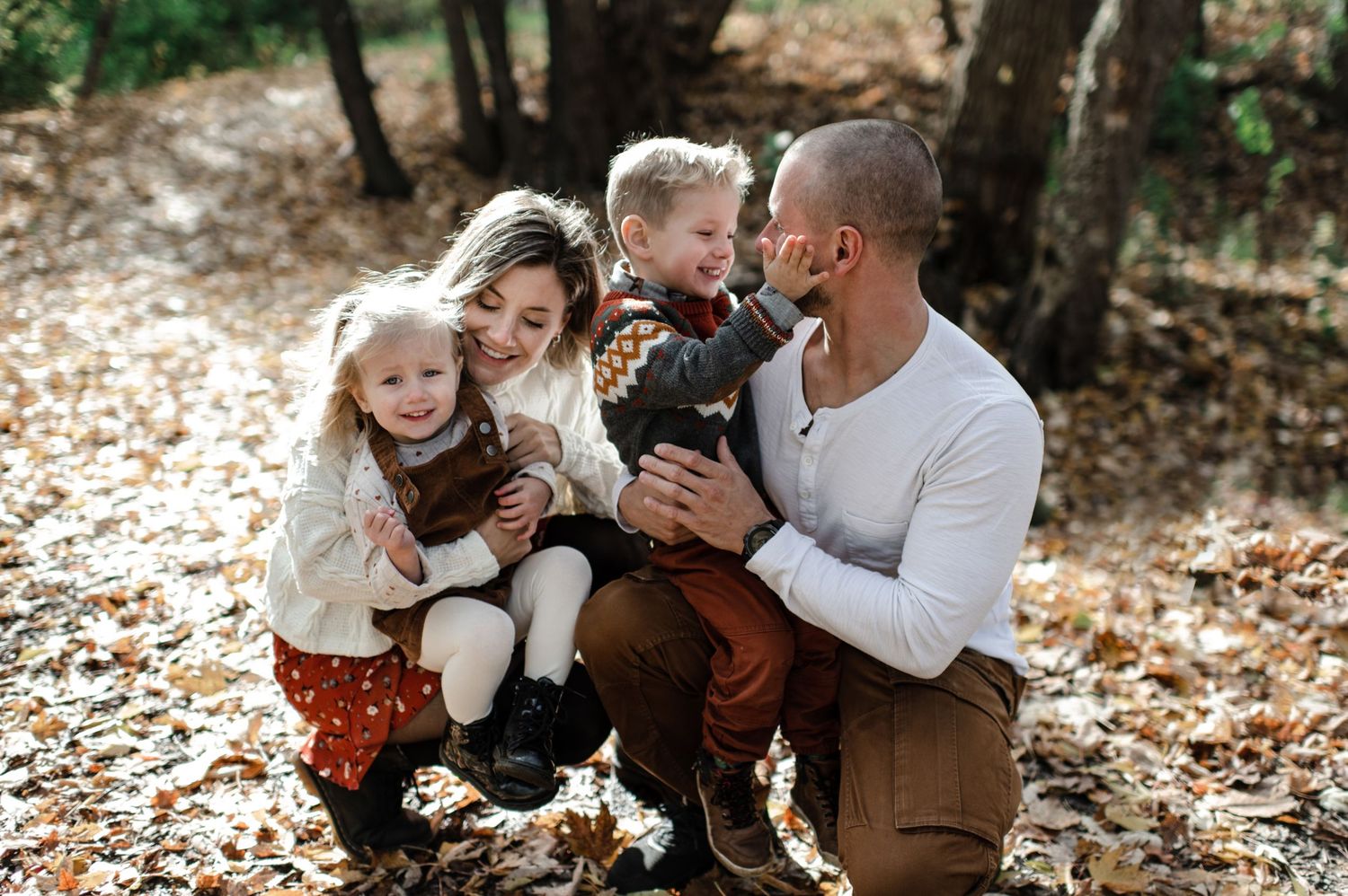 Happy family playing and laughing together while sitting on fallen autumn leaves.