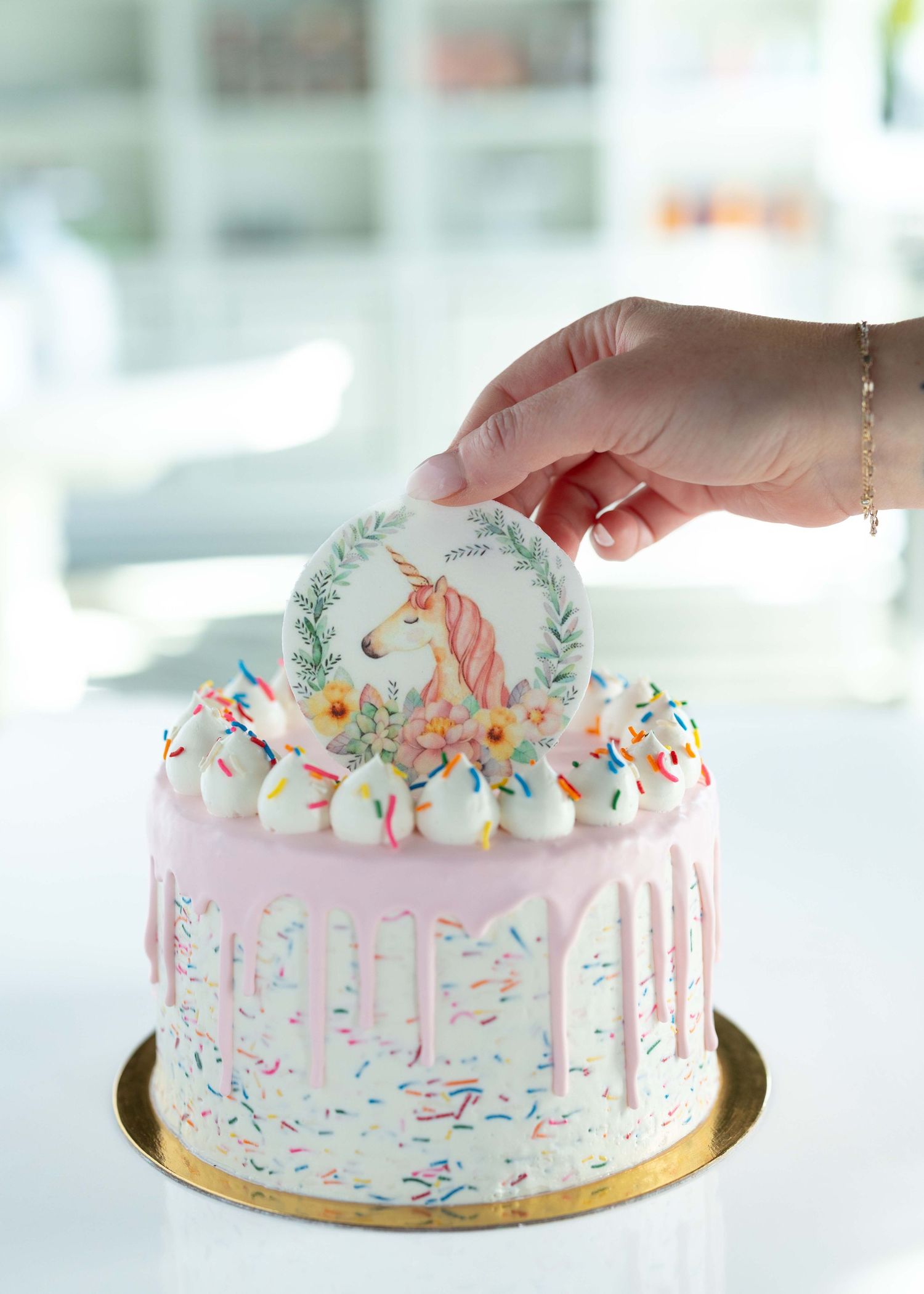 A pink unicorn-themed cake with drip icing, rainbow sprinkles, and gold accents shown from three different angles.