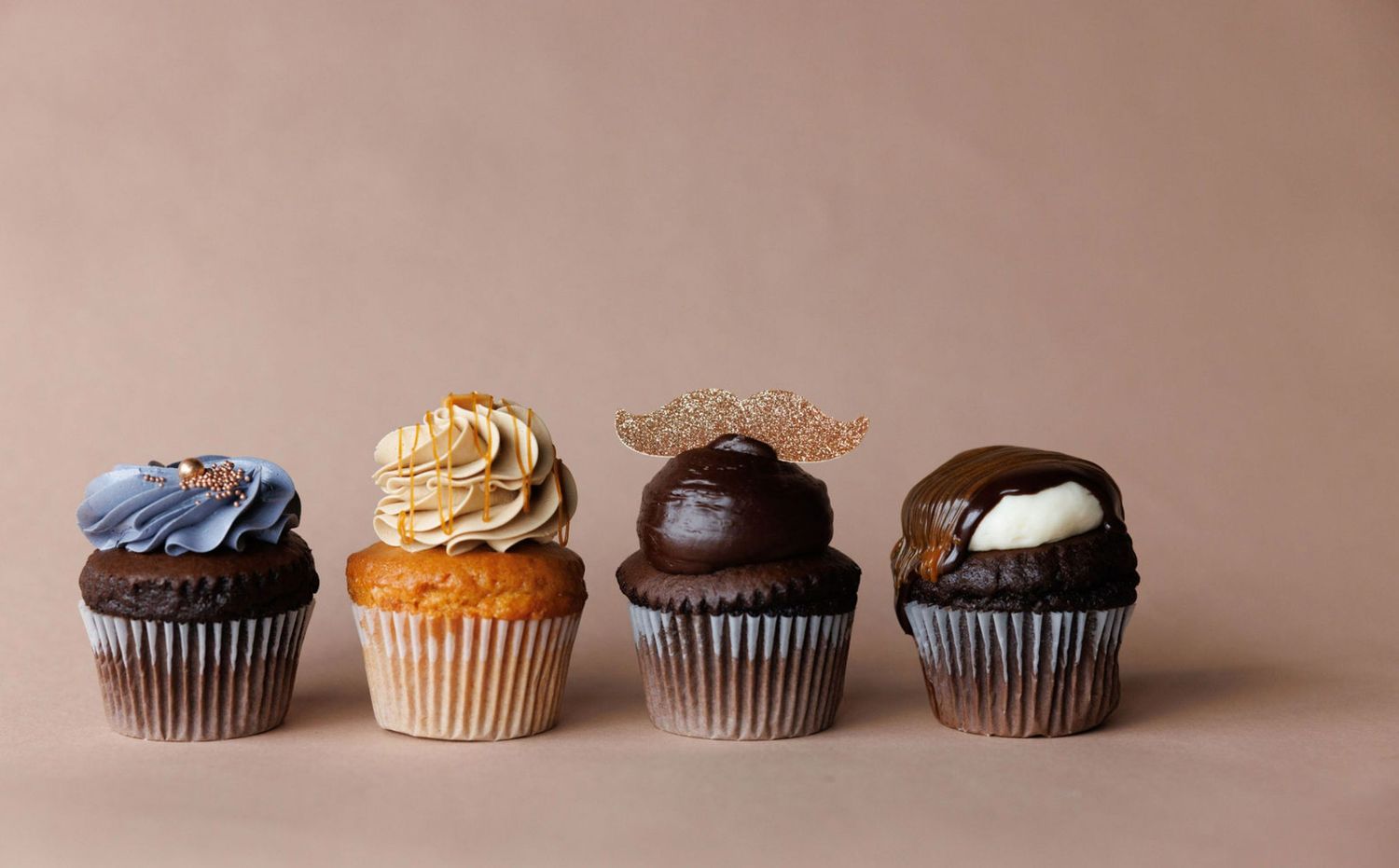 Row of chocolate and vanilla cupcakes with frosting on neutral background.