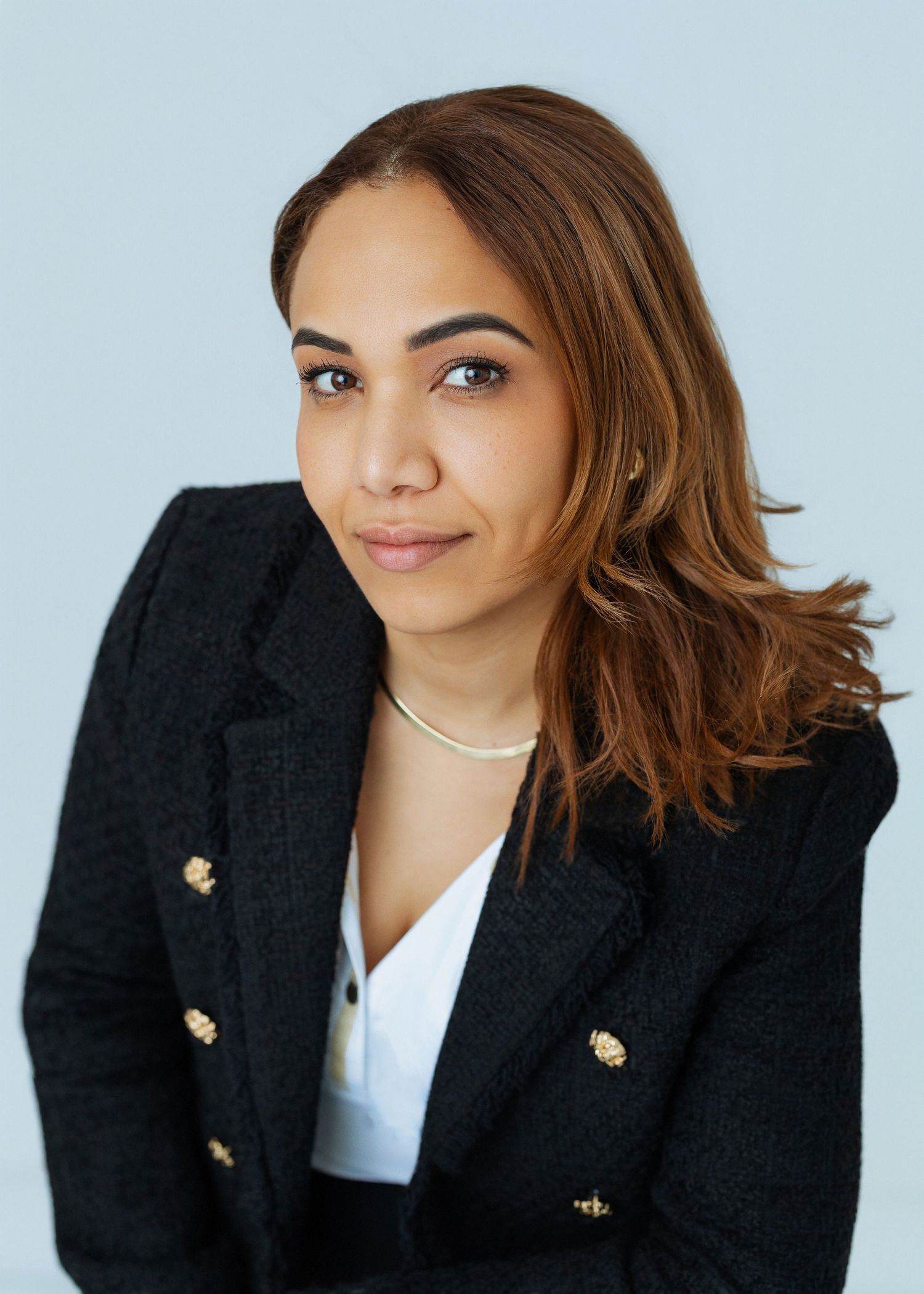 Professional headshot series showing different poses in a black blazer with gold buttons against a light blue background.