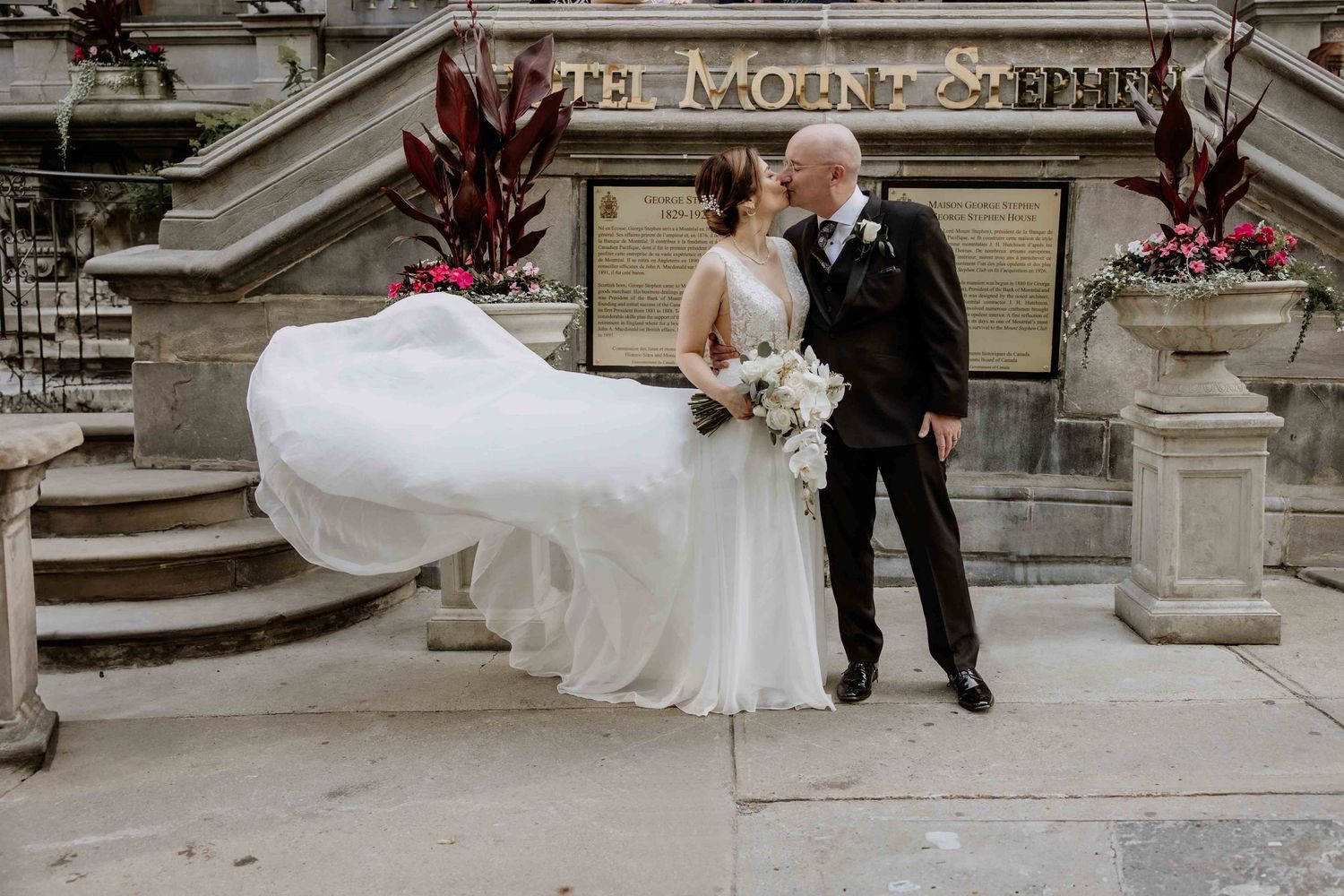 Wedding couple poses on historic stone steps with flowing veil.