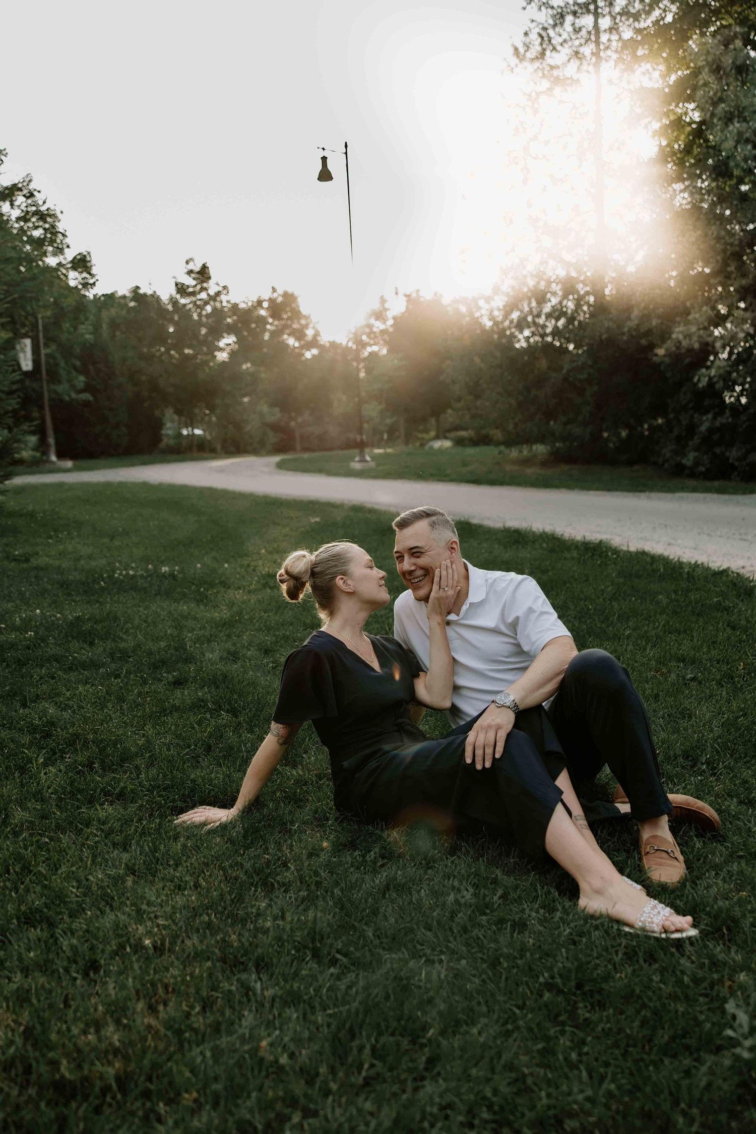 A couple relaxes on grass during sunset in a park setting.