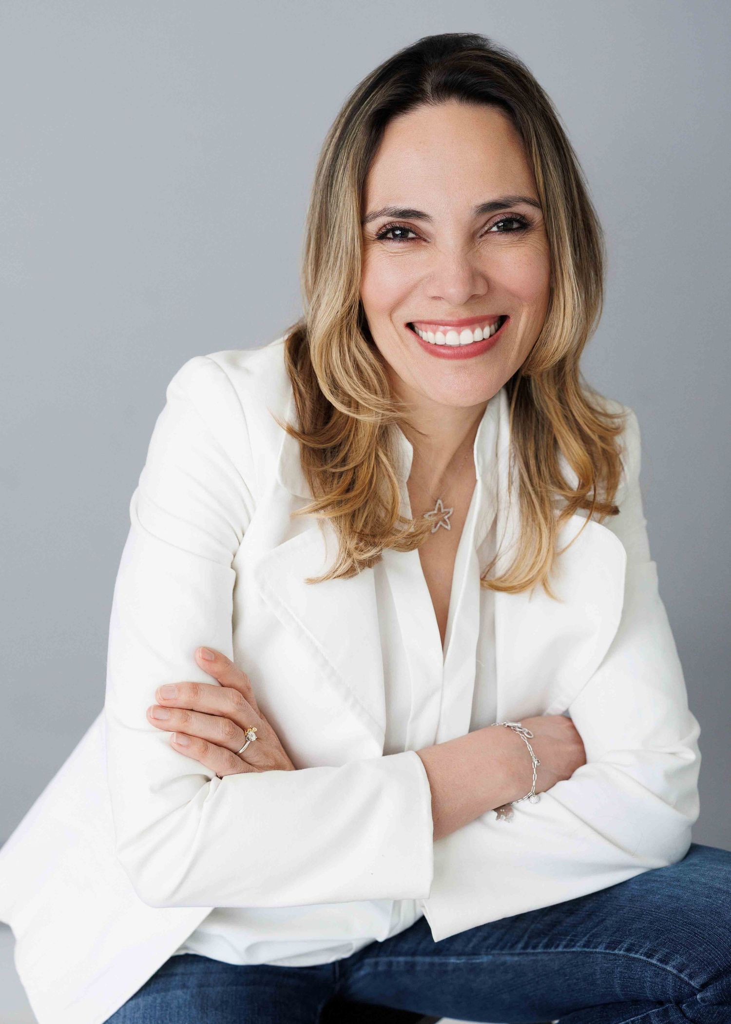 Professional headshot of person in white blazer against grey background.