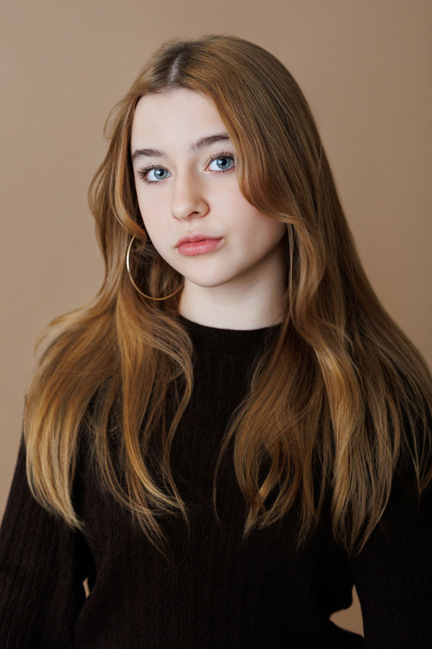 Portrait of young woman in black sweater with long wavy hair and gold hoop earrings.