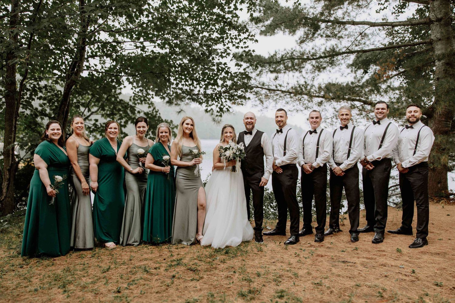 Large wedding party lined up outdoors wearing coordinated green and neutral attire.