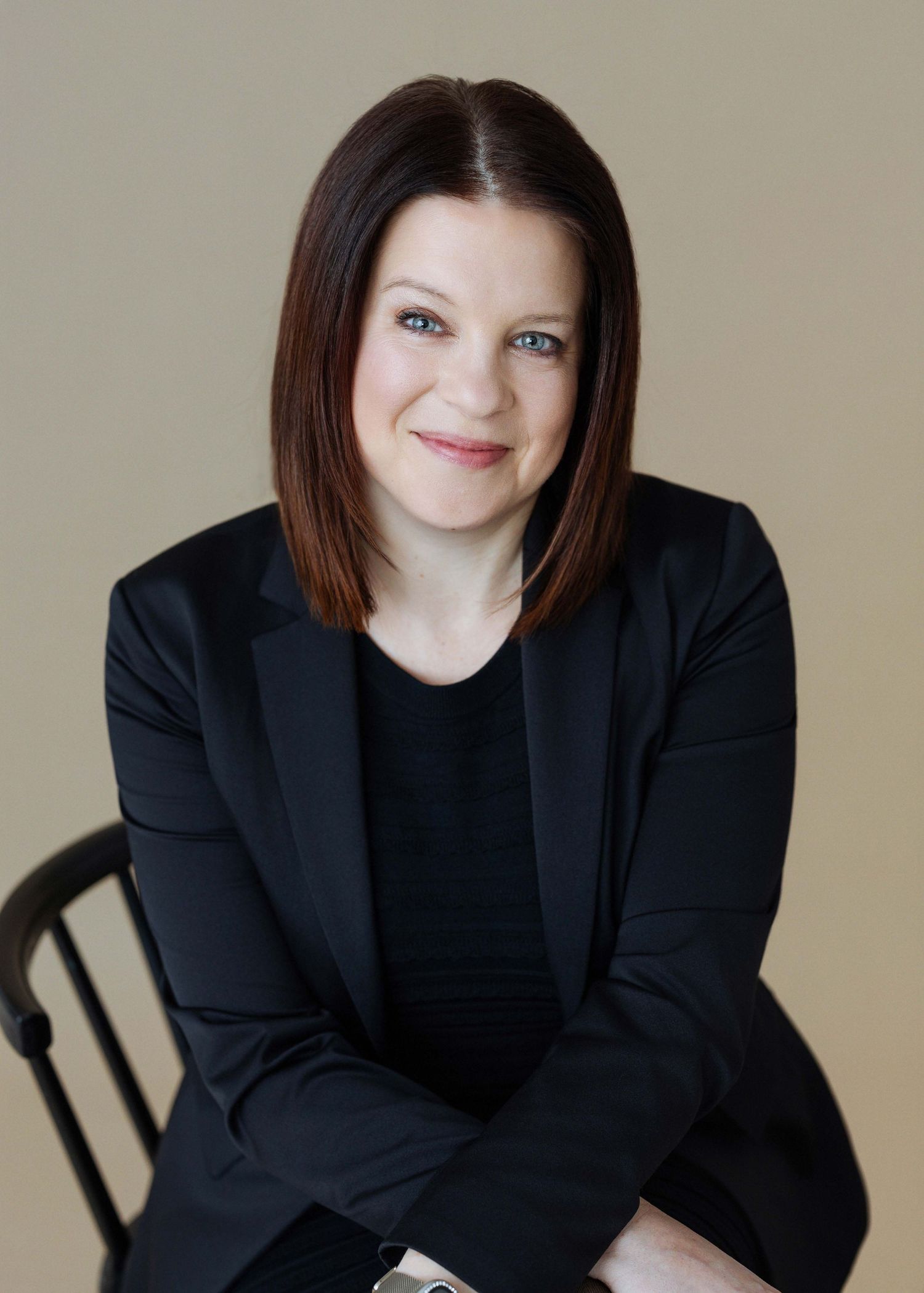 Professional portrait of someone in a black blazer seated against a neutral background.