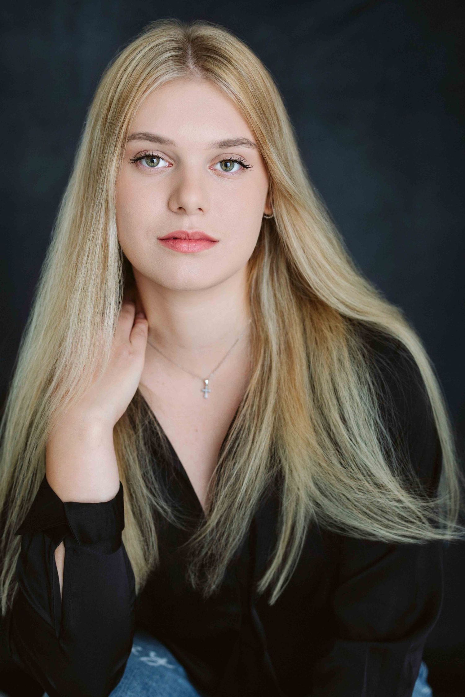 Studio portraits in black top showing blonde hair against dark background.