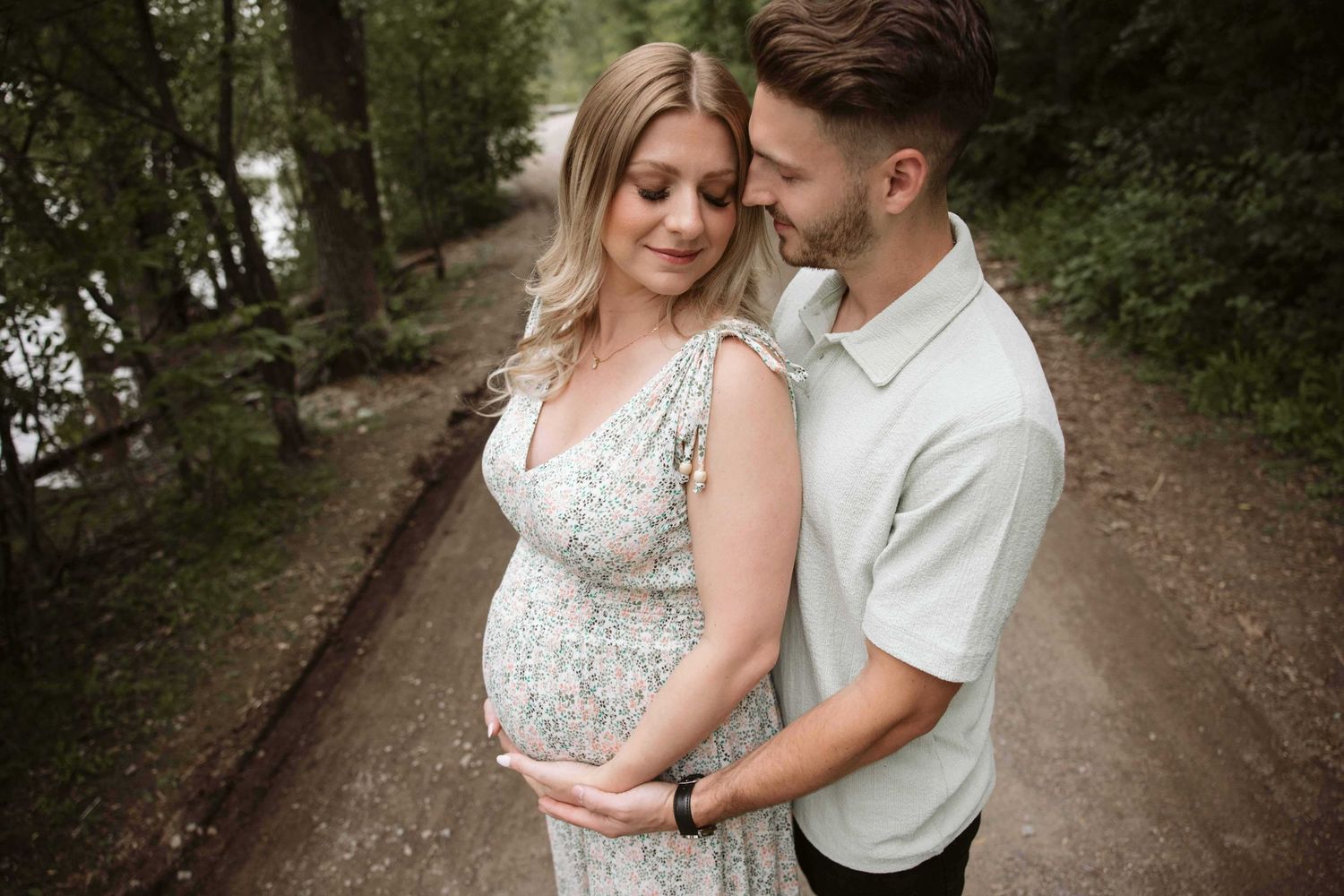 A tender maternity moment captured on a wooded path with natural lighting.