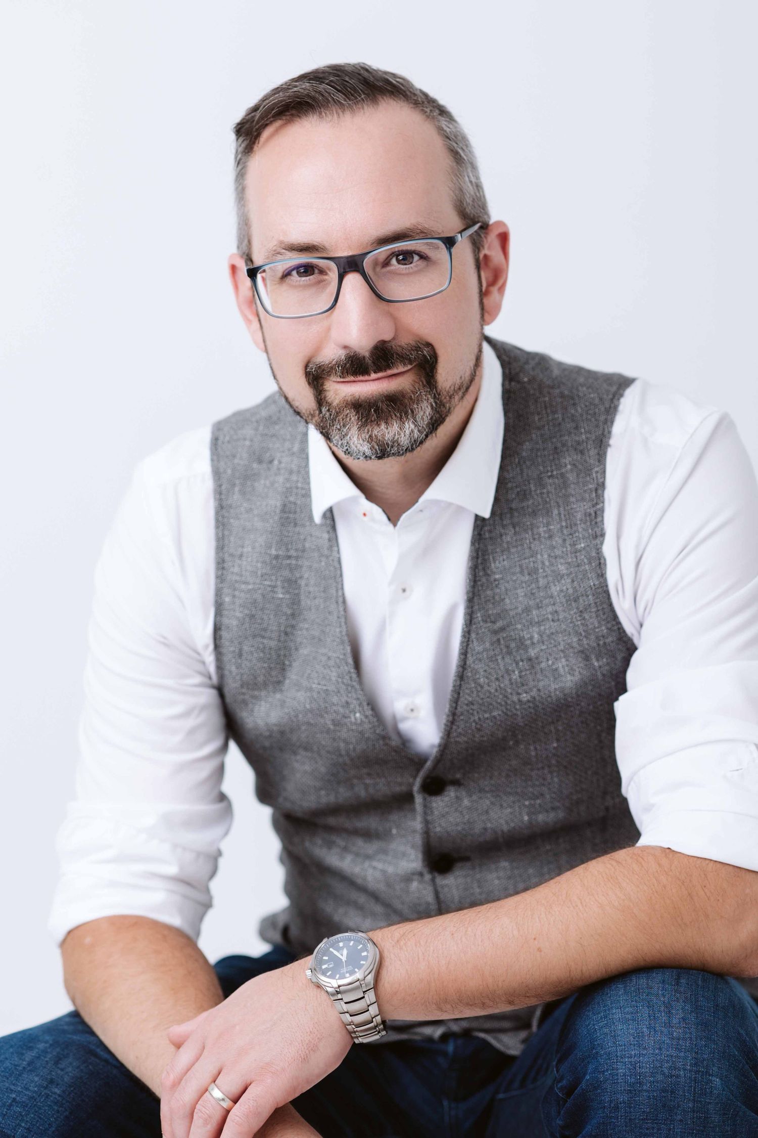 Professional headshots of person in grey vest and white shirt against light background.