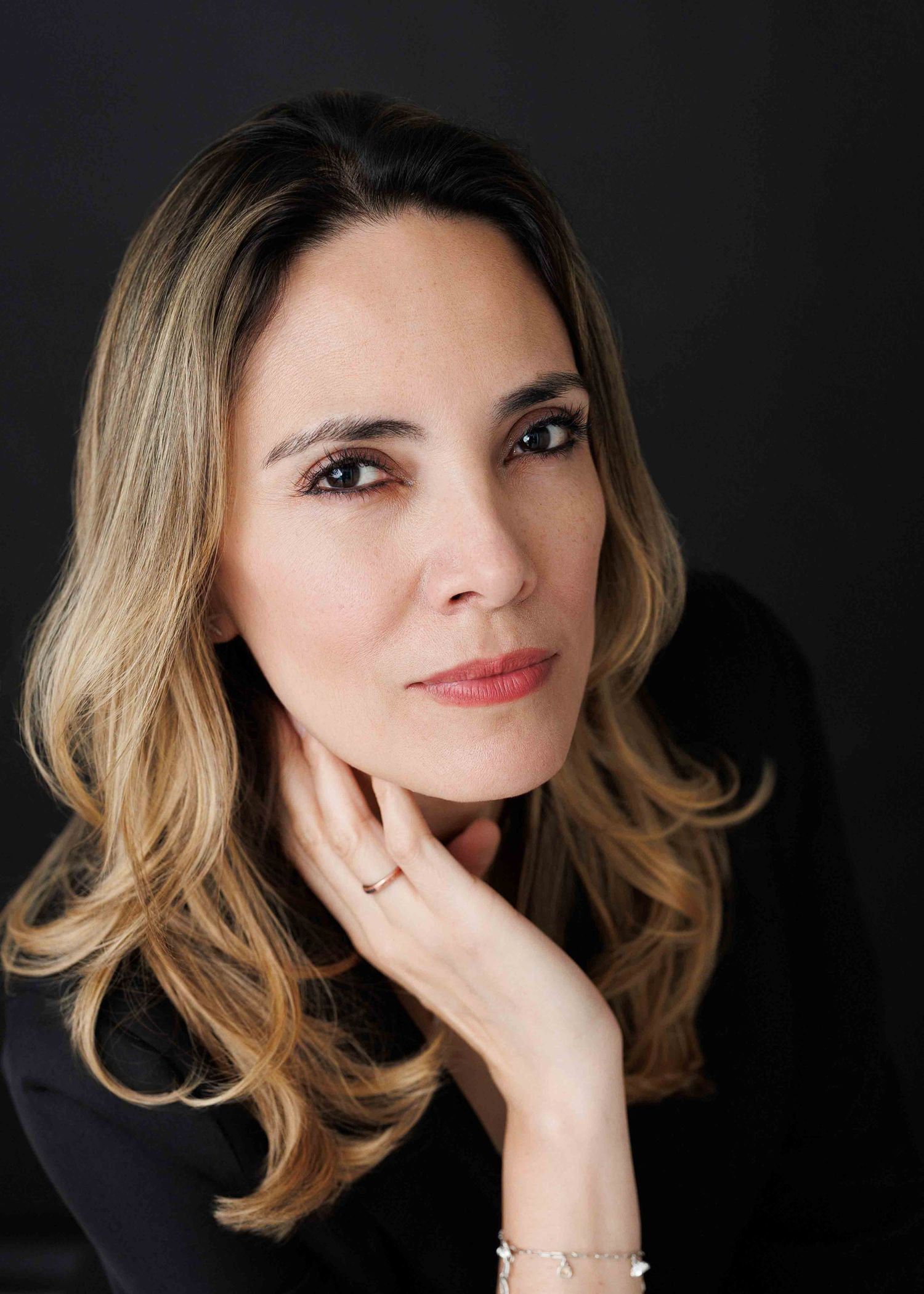 Stylish professional portraits with wavy hair and black blazer against dark backdrop.