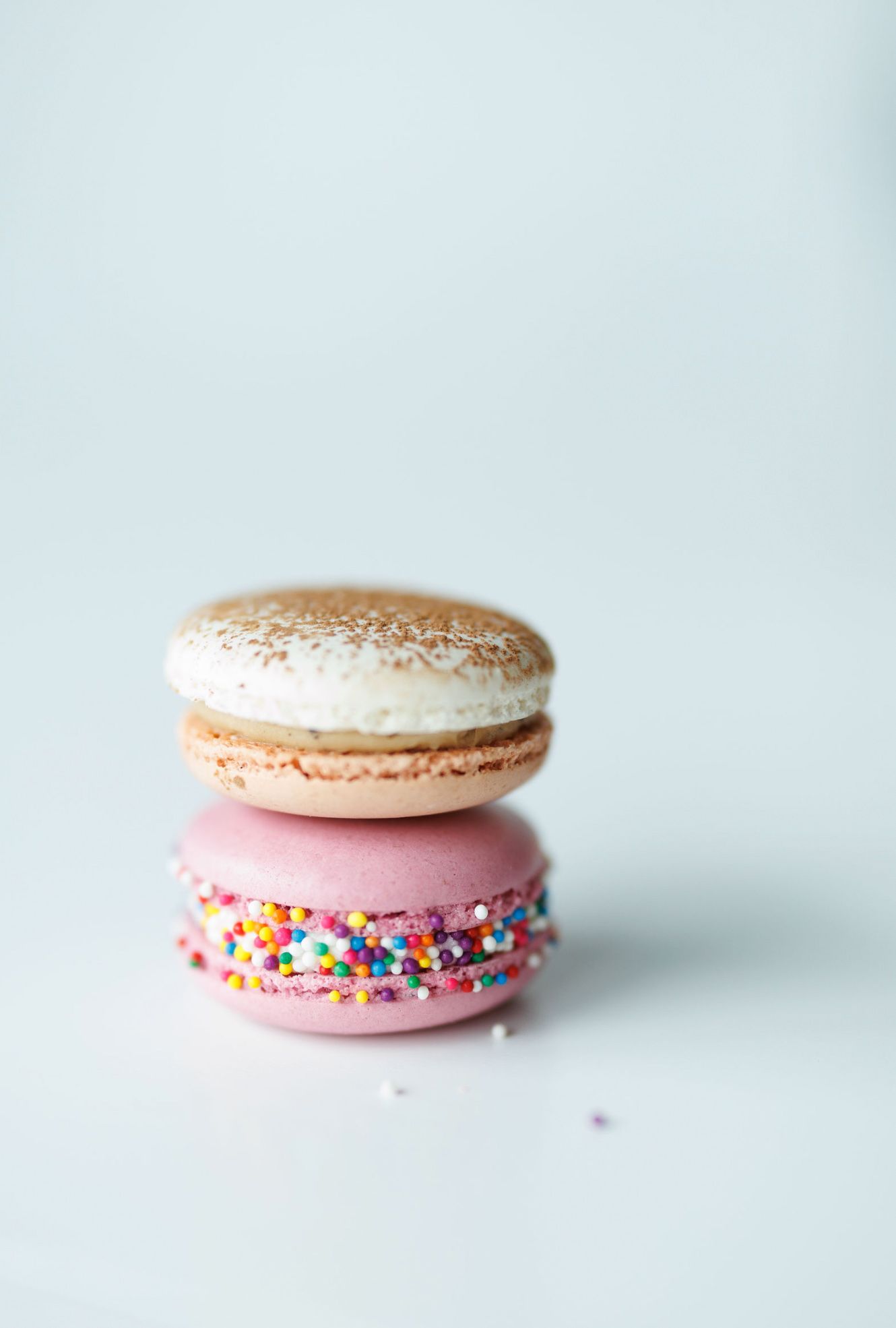 Pink macaron with rainbow sprinkles on white background.
