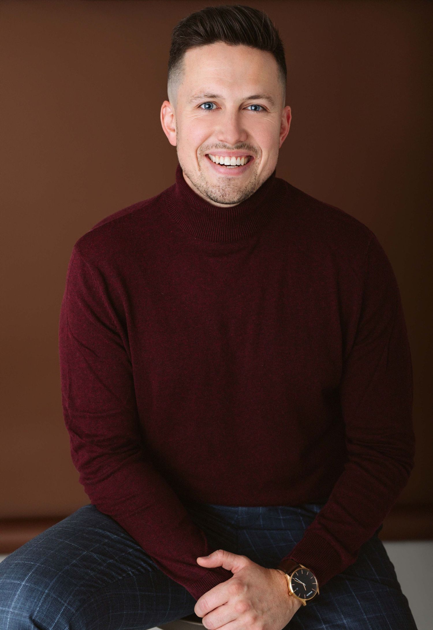 Professional portrait of someone in a burgundy turtleneck sweater against a dark backdrop.