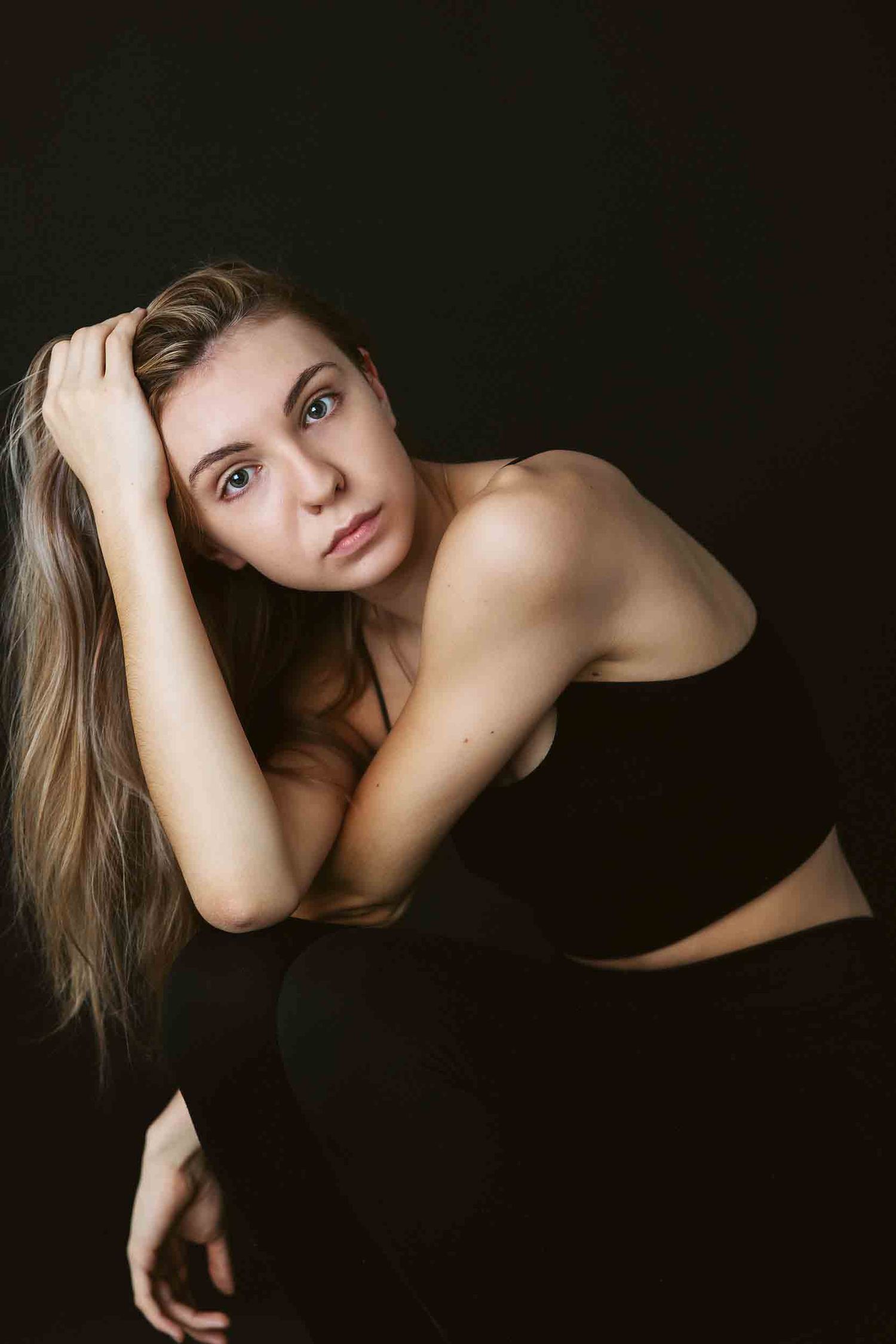 Artistic portrait against dark background showing contemplative pose in black outfit.