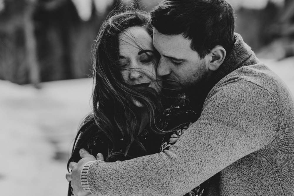 A tender black and white photograph showing a couple embracing in soft natural light.