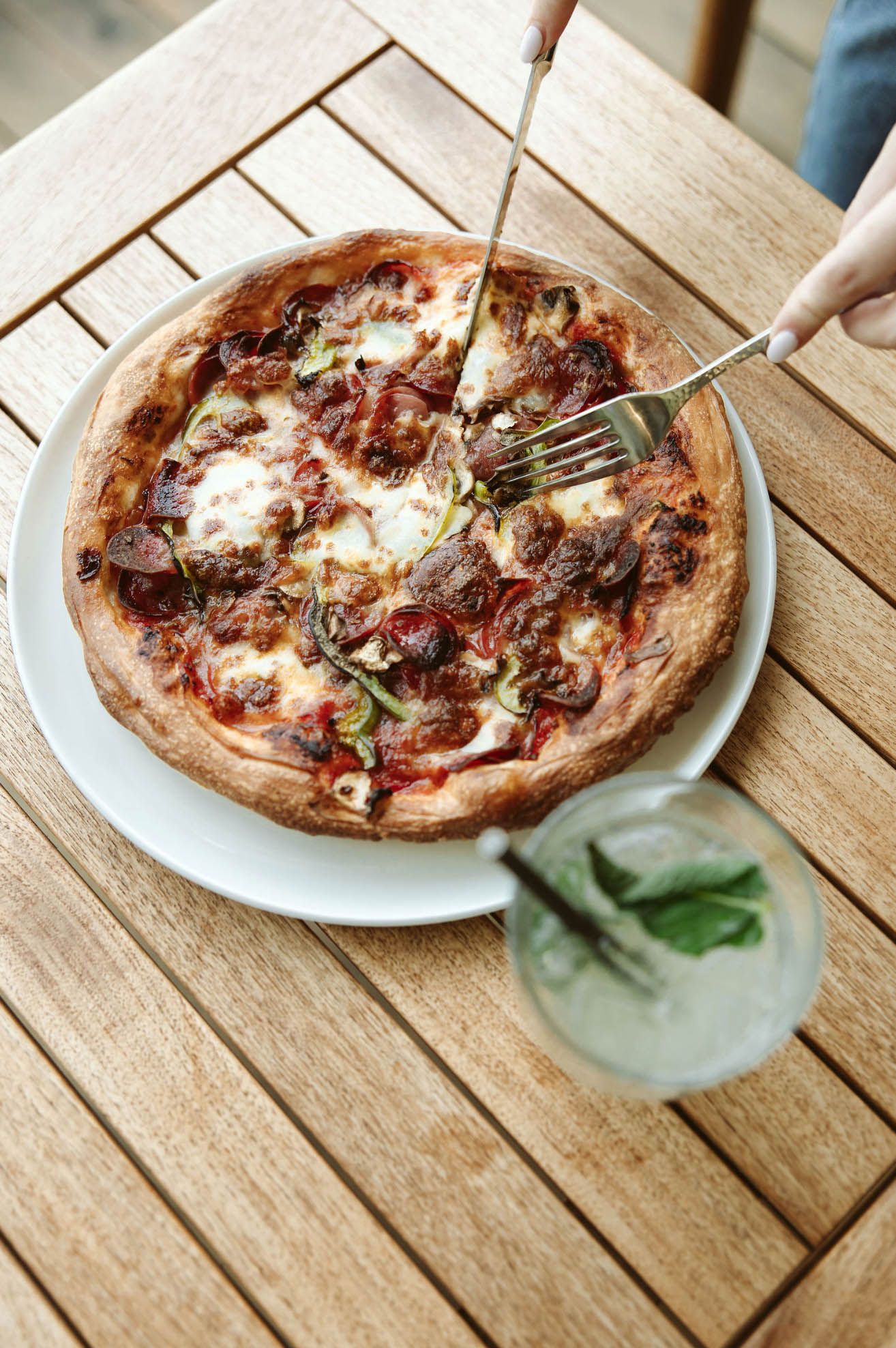 Wood-fired pizza with melted cheese and herbs on rustic wooden table.