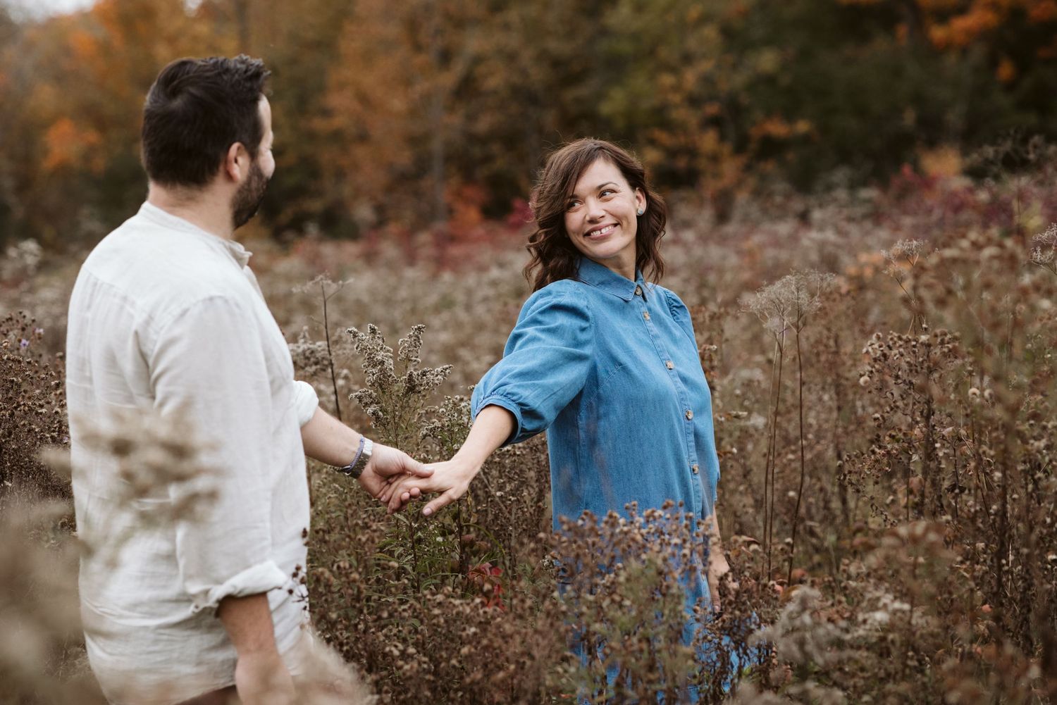 Two people dance and play in a field during autumn with warm fall colors in the background.
