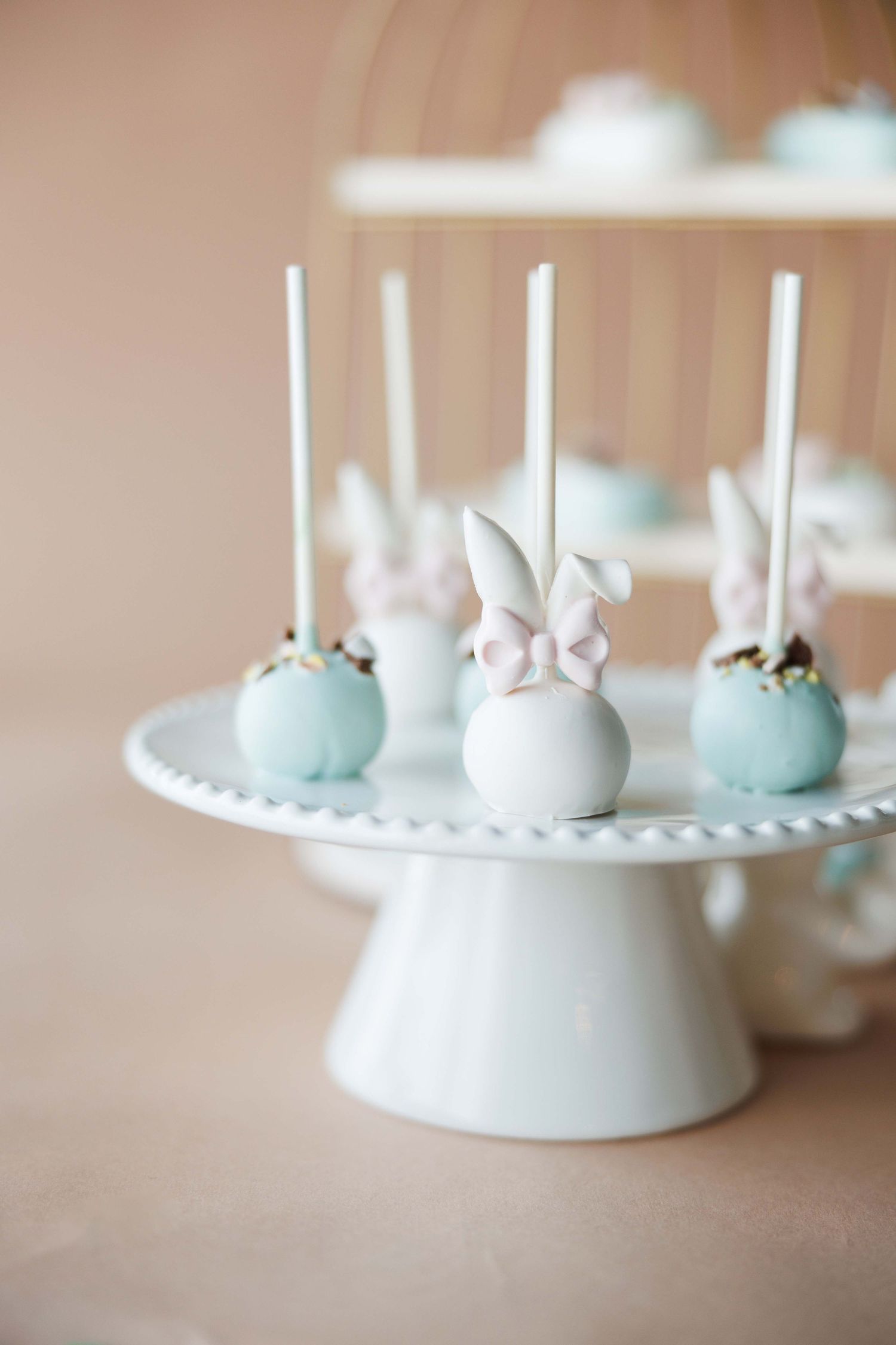 Pastel cake pops displayed on a white circular stand with delicate details.