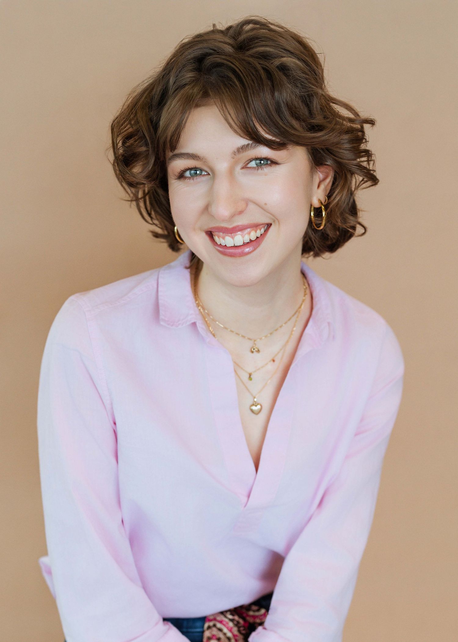 A person in a pink blazer and necklace poses against a beige background in a series of four similar shots.