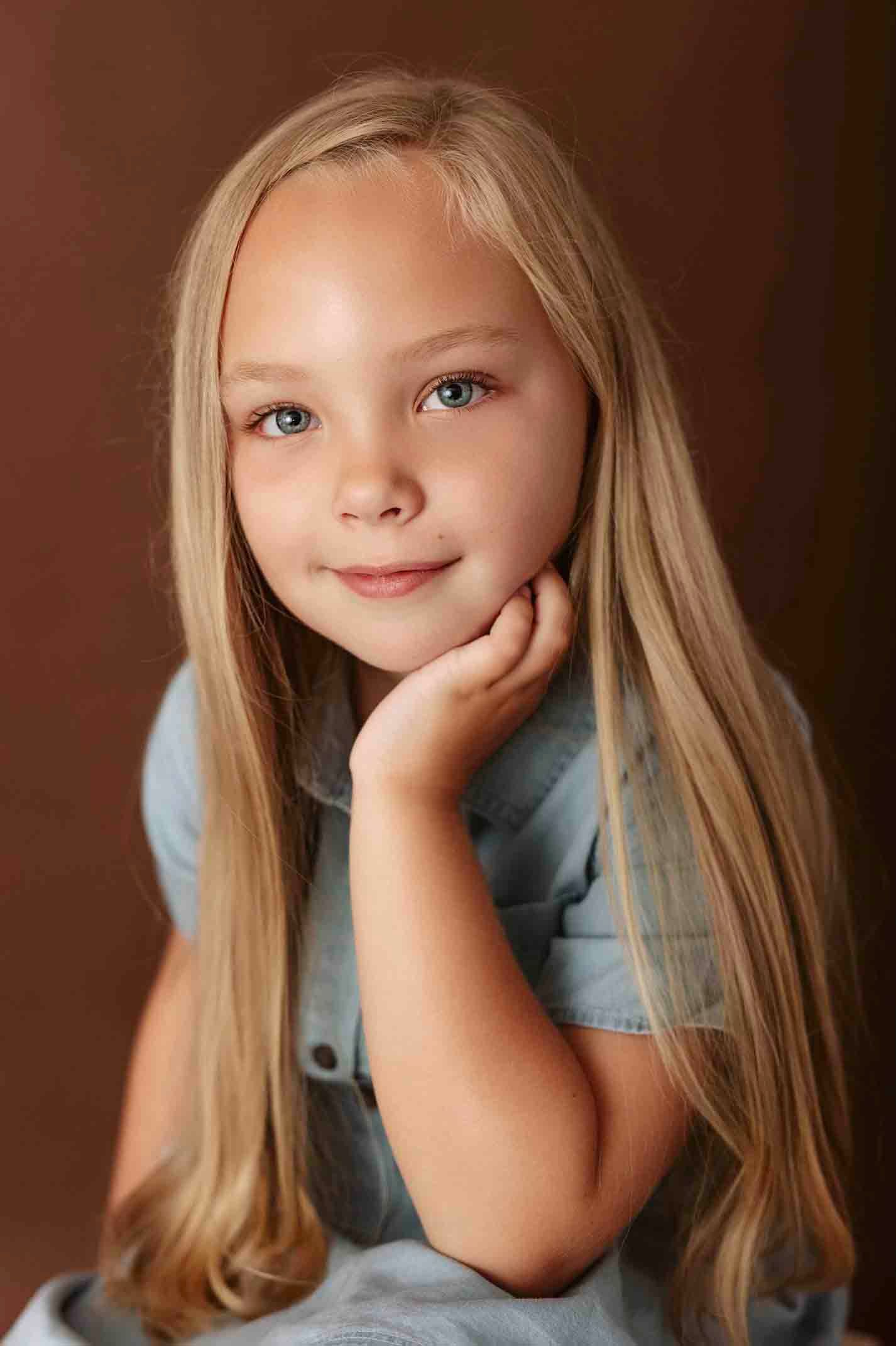 Child in denim outfit posing for studio portraits against dark background.