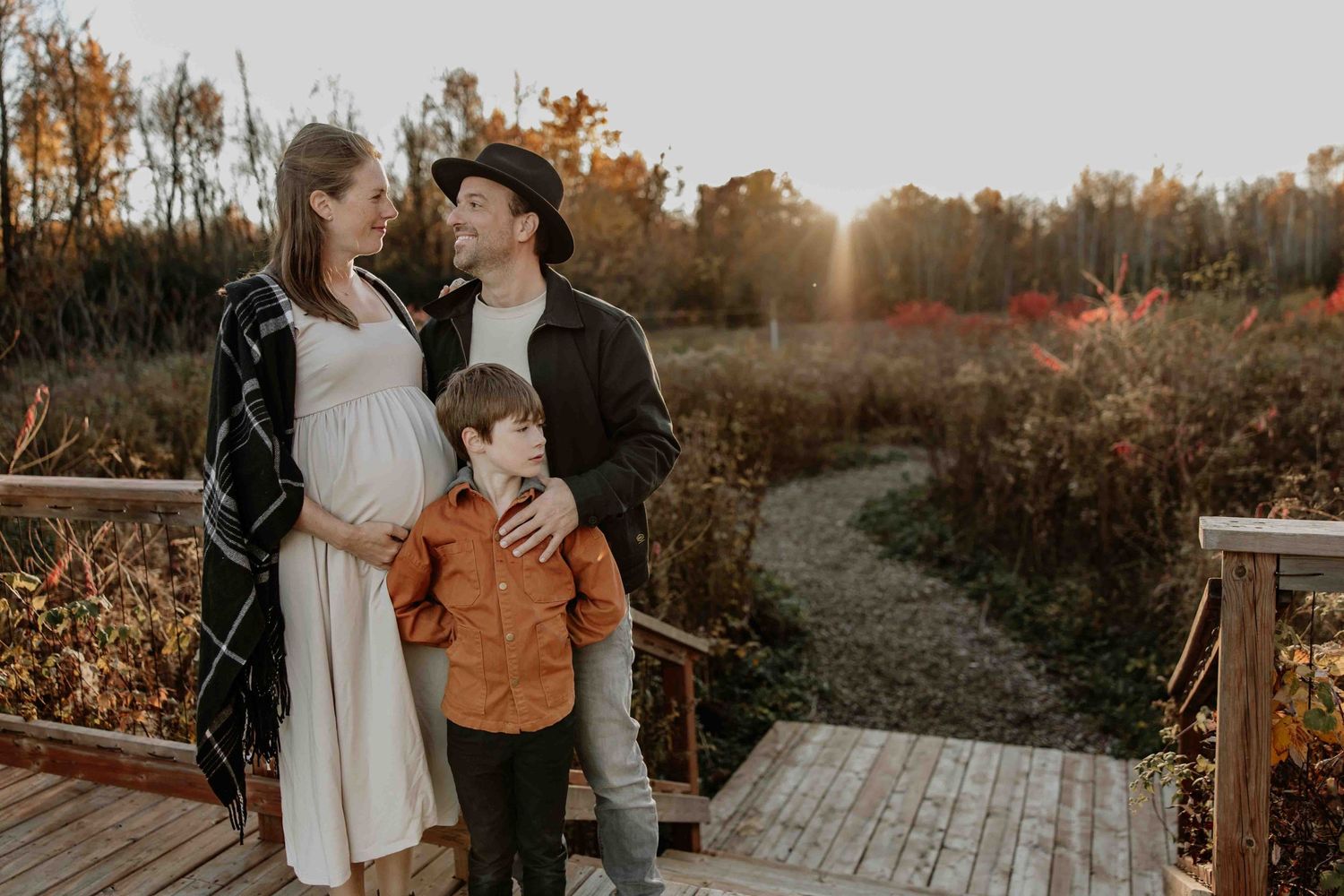 Family standing together on wooden deck surrounded by autumn foliage at golden hour.