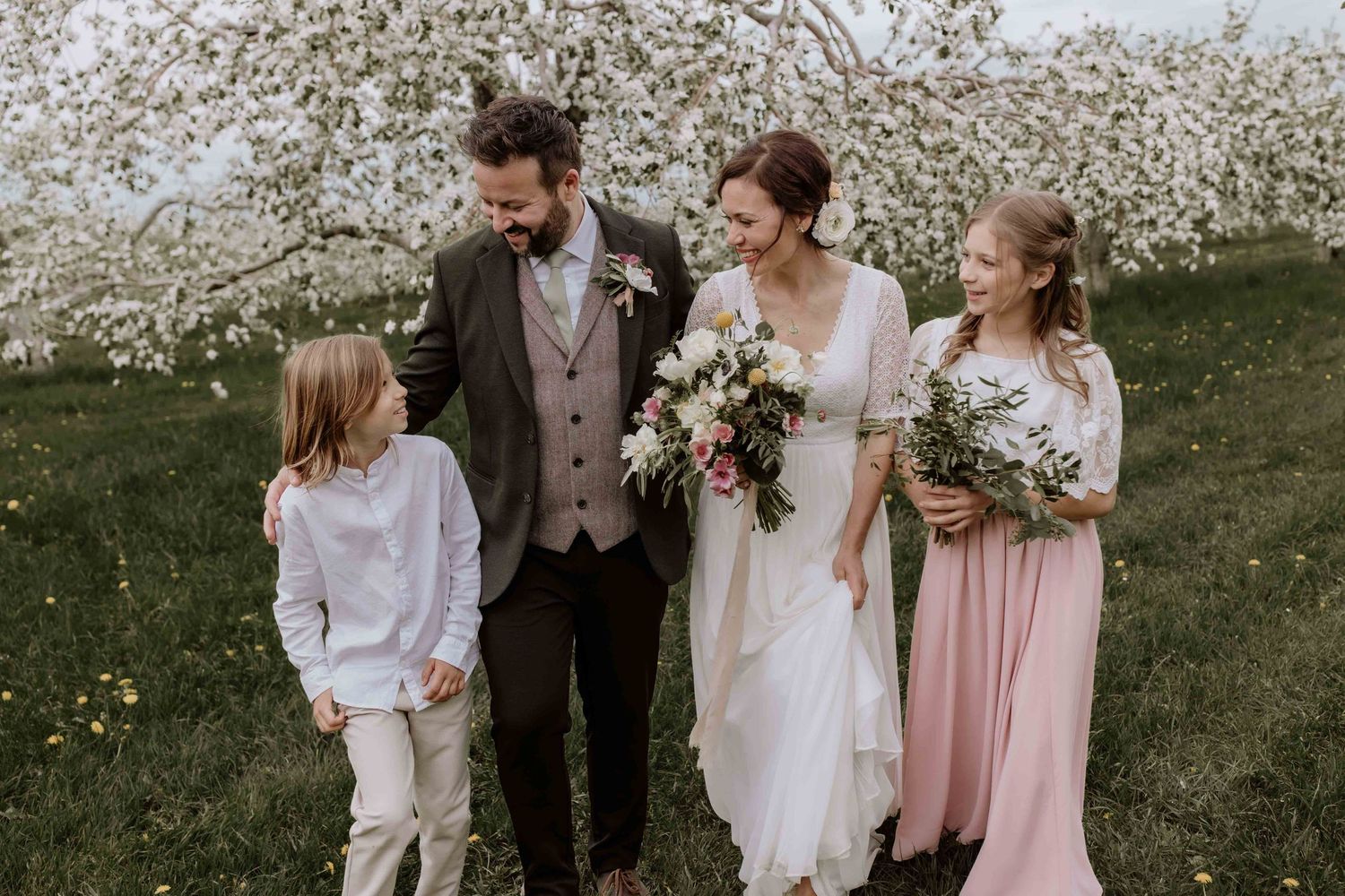 Wedding party in soft pink and white attire gathered for outdoor spring photos.