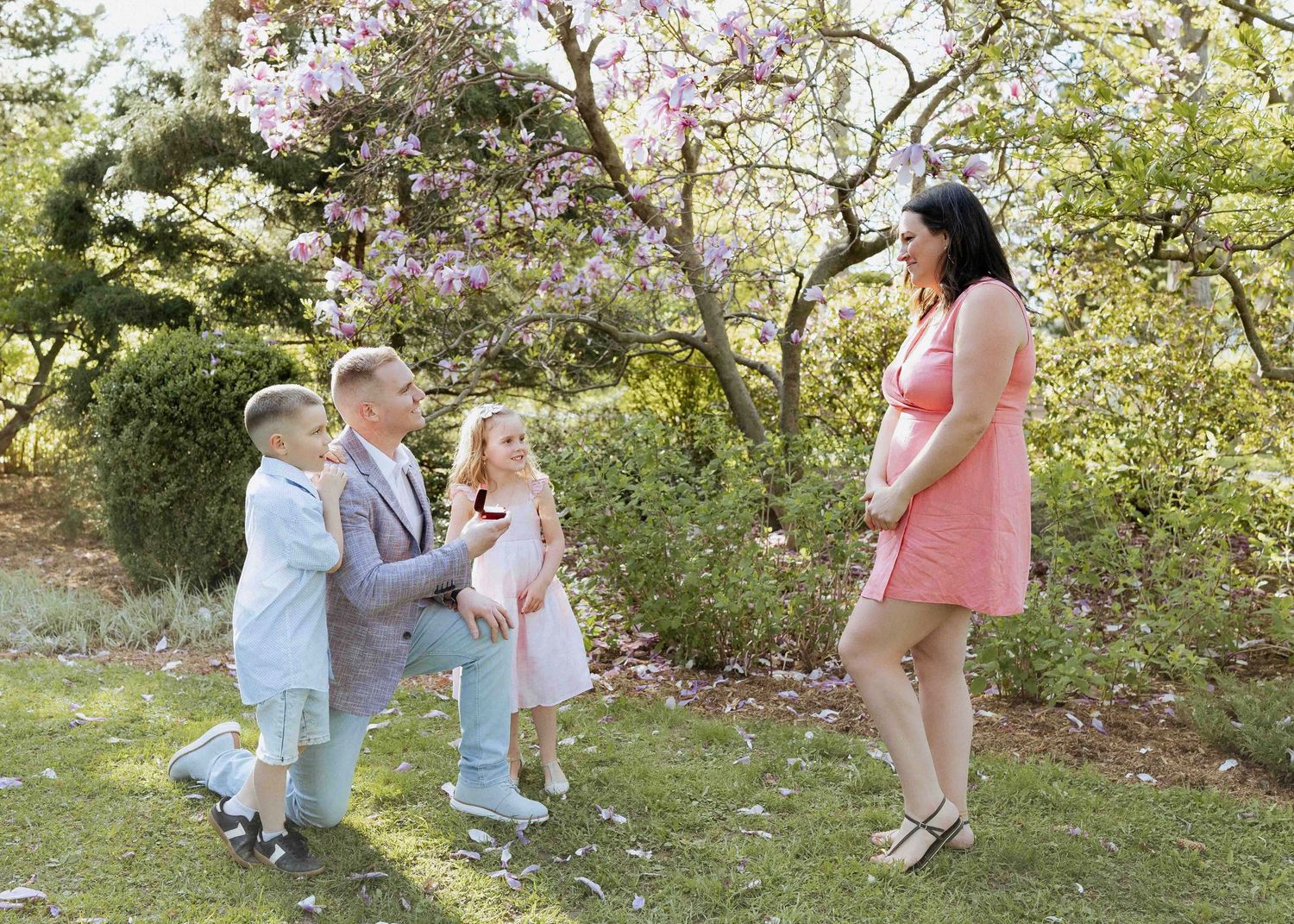Family photo session with parents and two children in a blooming garden with purple flowering trees.