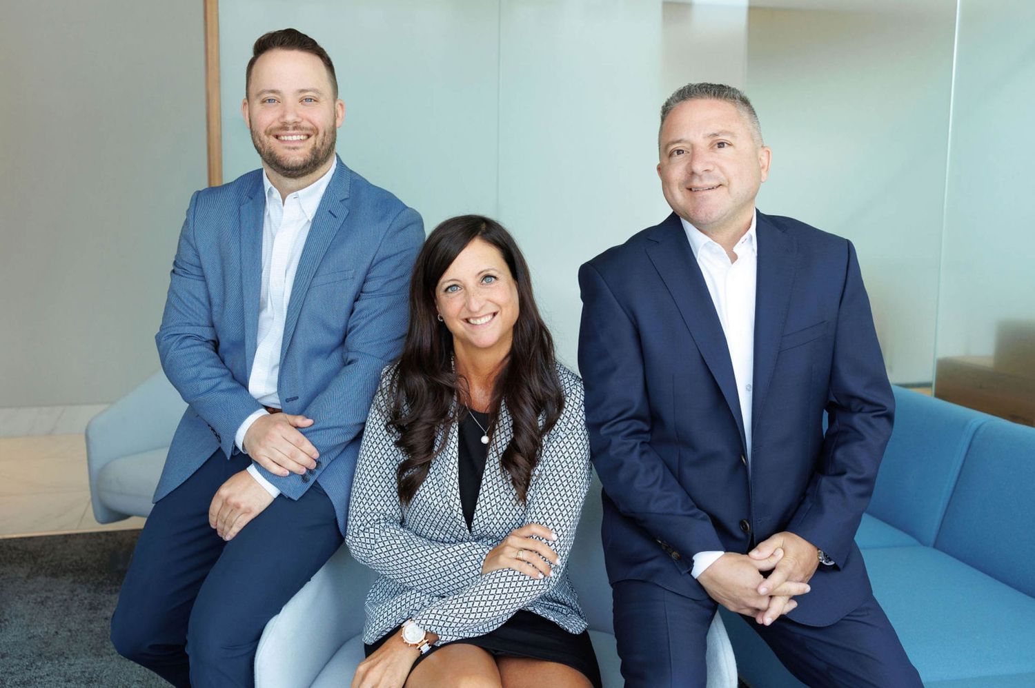 Professional business team members sitting on blue couch during office meeting.