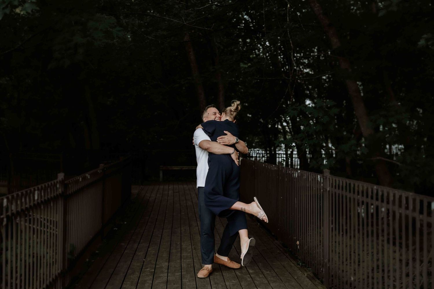 Romantic silhouettes embrace on a wooden bridge at dusk.