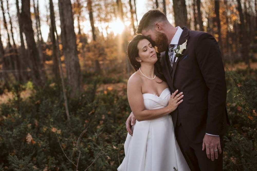 A romantic sunset wedding photo of newlyweds embracing in an autumn forest.