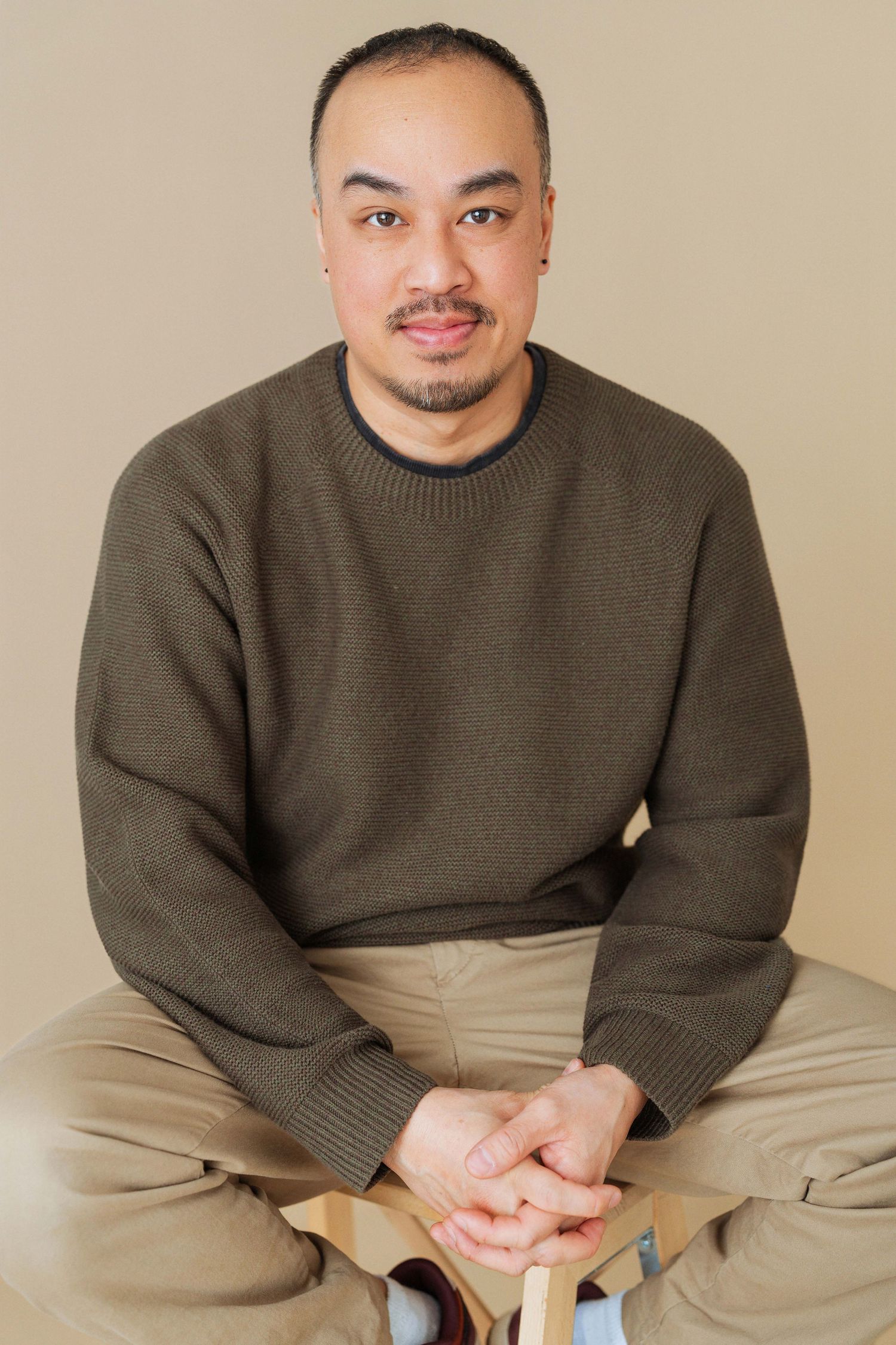 A person in an olive green sweater and khaki pants sits casually in a series of connected poses.