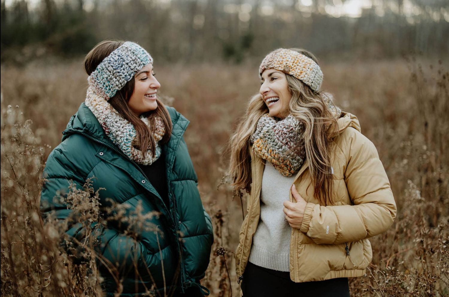 Two people in winter coats and knit hats sharing laughter outdoors in a field.
