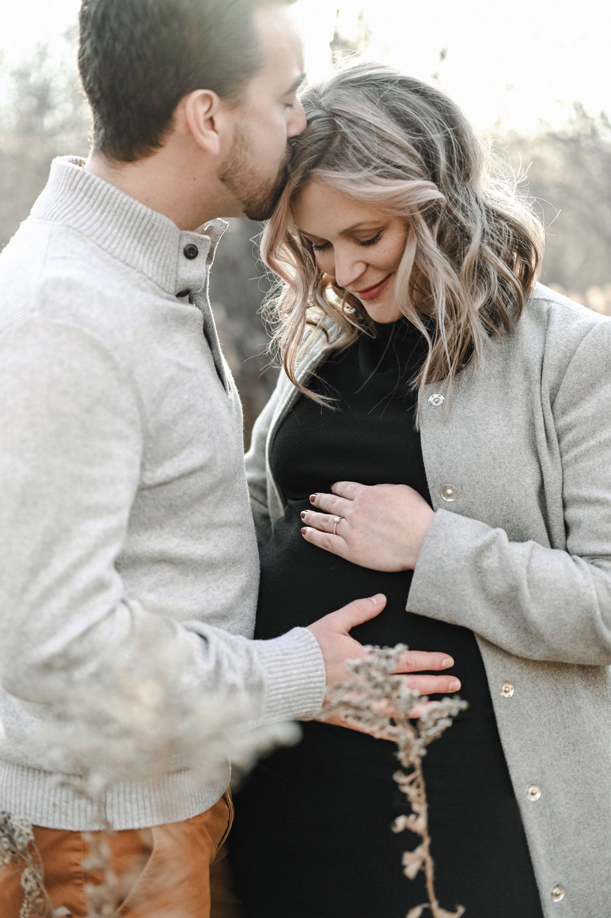 Couple in grey and black sharing intimate moment during winter maternity session.