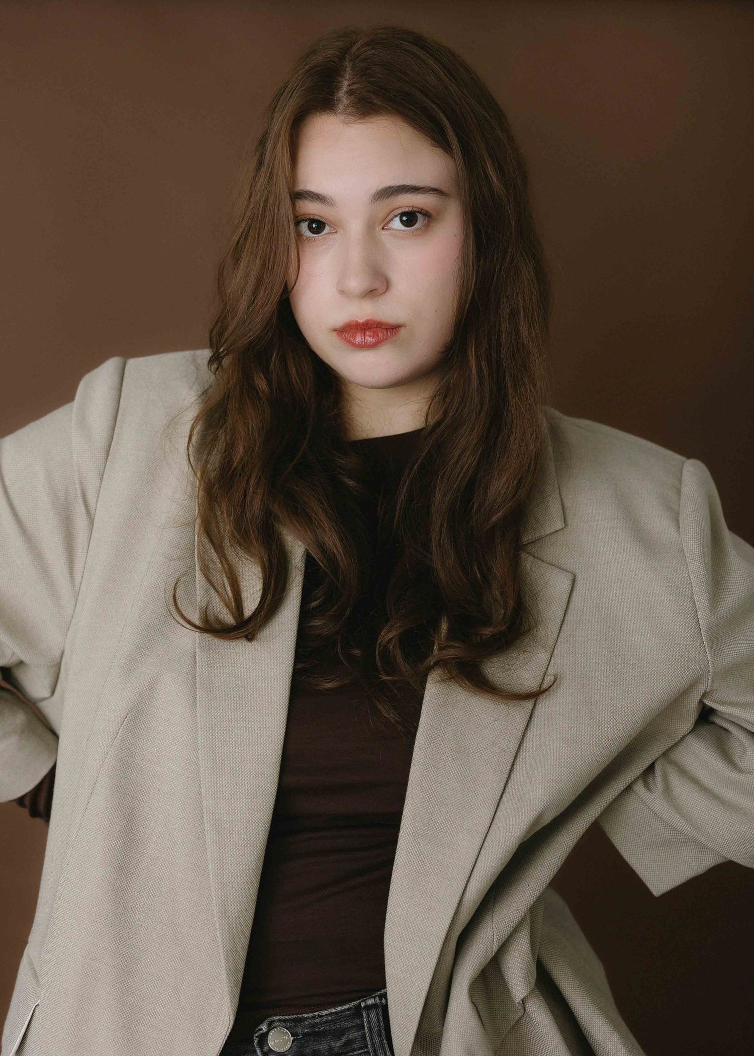Fashion portrait series featuring an oversized beige blazer and dark top against brown backdrop.